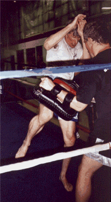Muay Thai fighter kicking pad held by a trainer in a boxing ring.