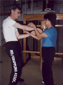 Four people pose inside a boxing ring. A man in black stands with two others who have arms around him. The fourth stands to the side.