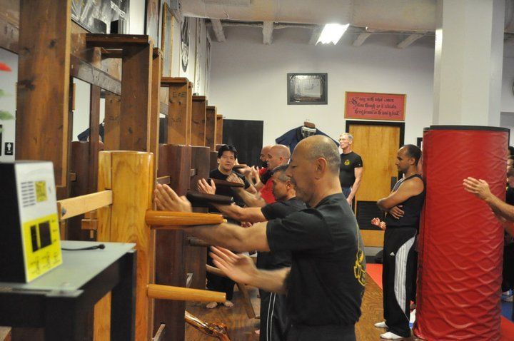 People practicing Wing Chun, striking wooden dummies in a martial arts studio.
