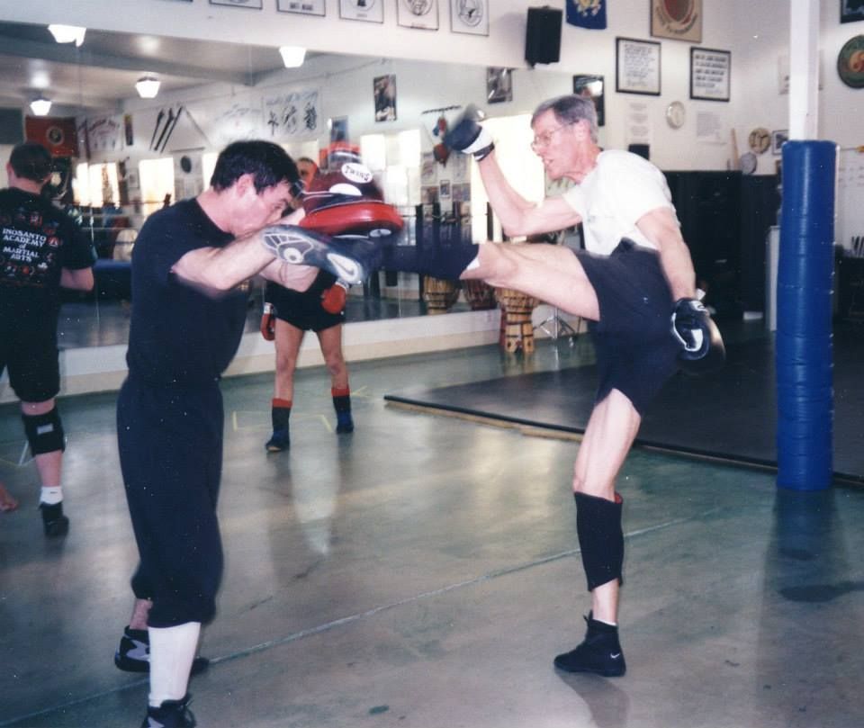 Man kicks pad held by another man in a gym, practicing martial arts.