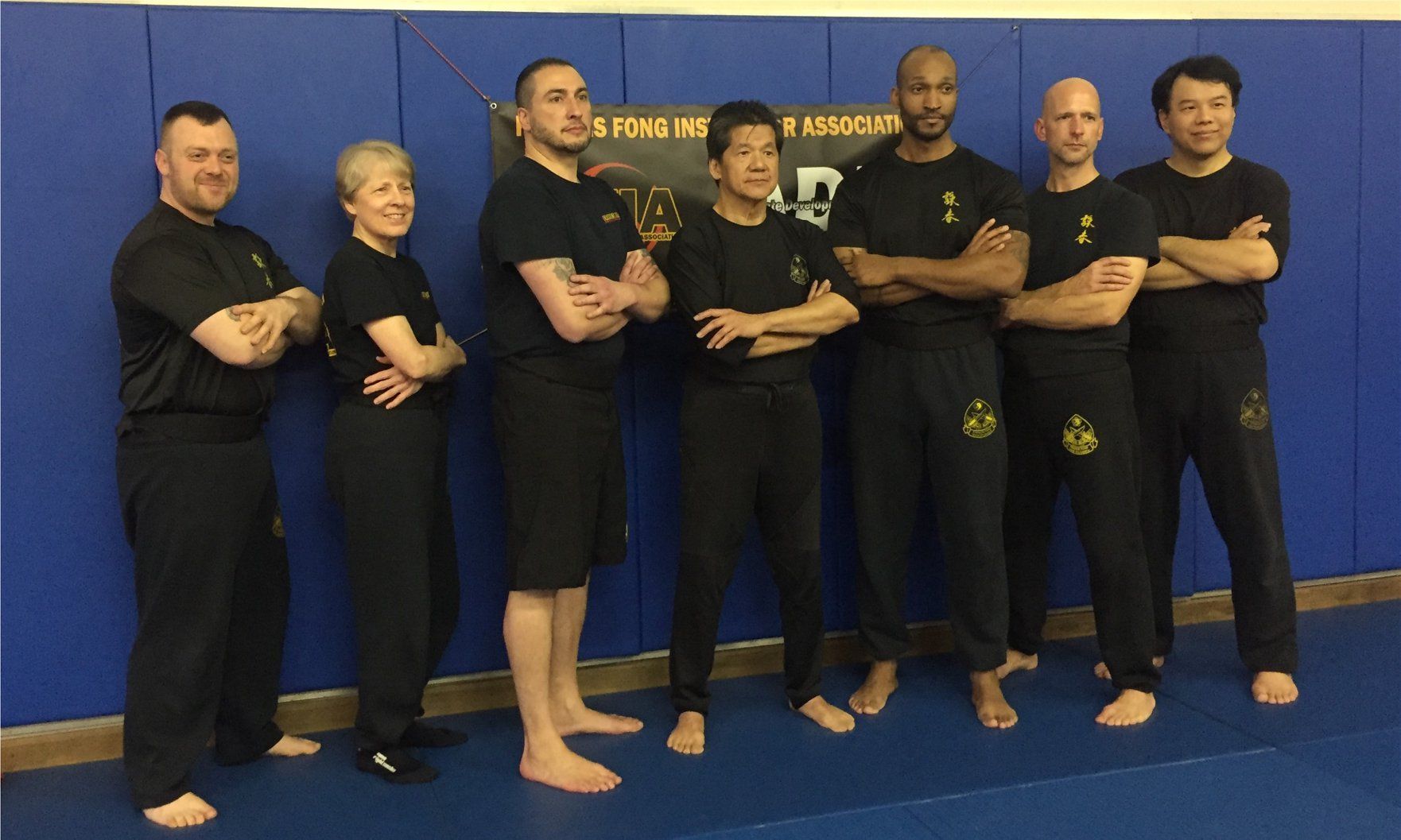 Group of people in black shirts and pants, arms crossed, in a martial arts setting, posing for a photo.