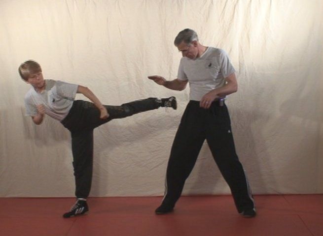 Person kicking in martial arts training; partner positioned nearby; light background.