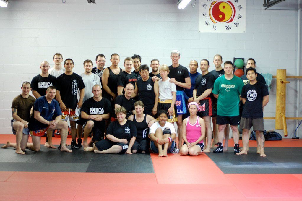 Group of people in a martial arts studio posing for a photo. They are wearing athletic attire.
