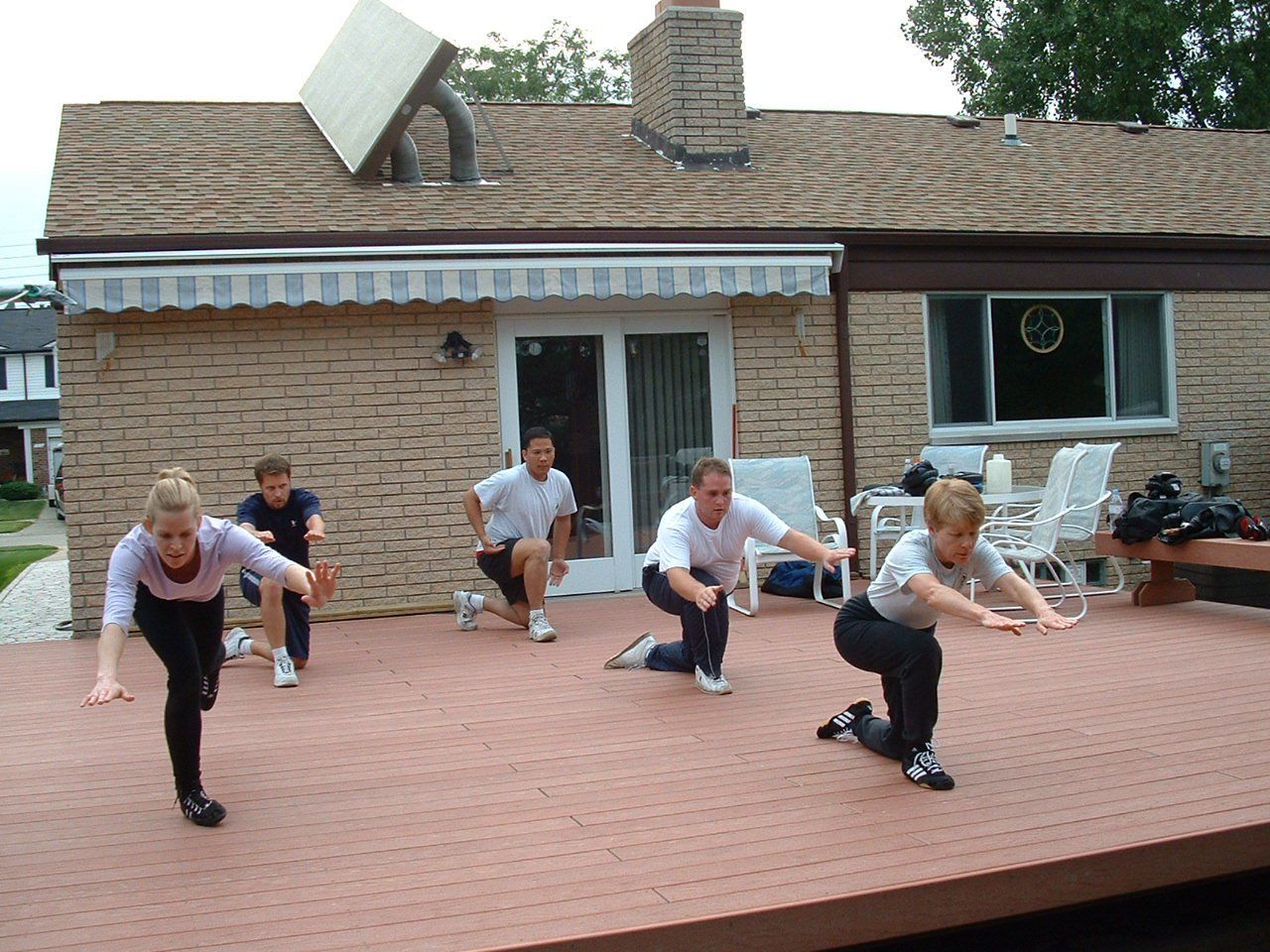 People doing lunges on a wooden deck in front of a house.