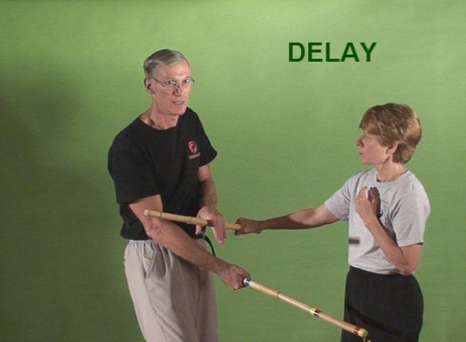 Two people practicing stick fighting, green background. Man holding sticks, the word 