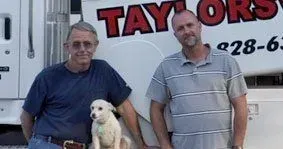 Two men are standing next to each other with a dog in front of a truck.