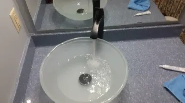 A black faucet running water into a frosted glass bowl sink on a speckled blue countertop.