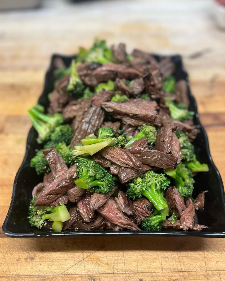 A black plate topped with steak and broccoli on a wooden table.
