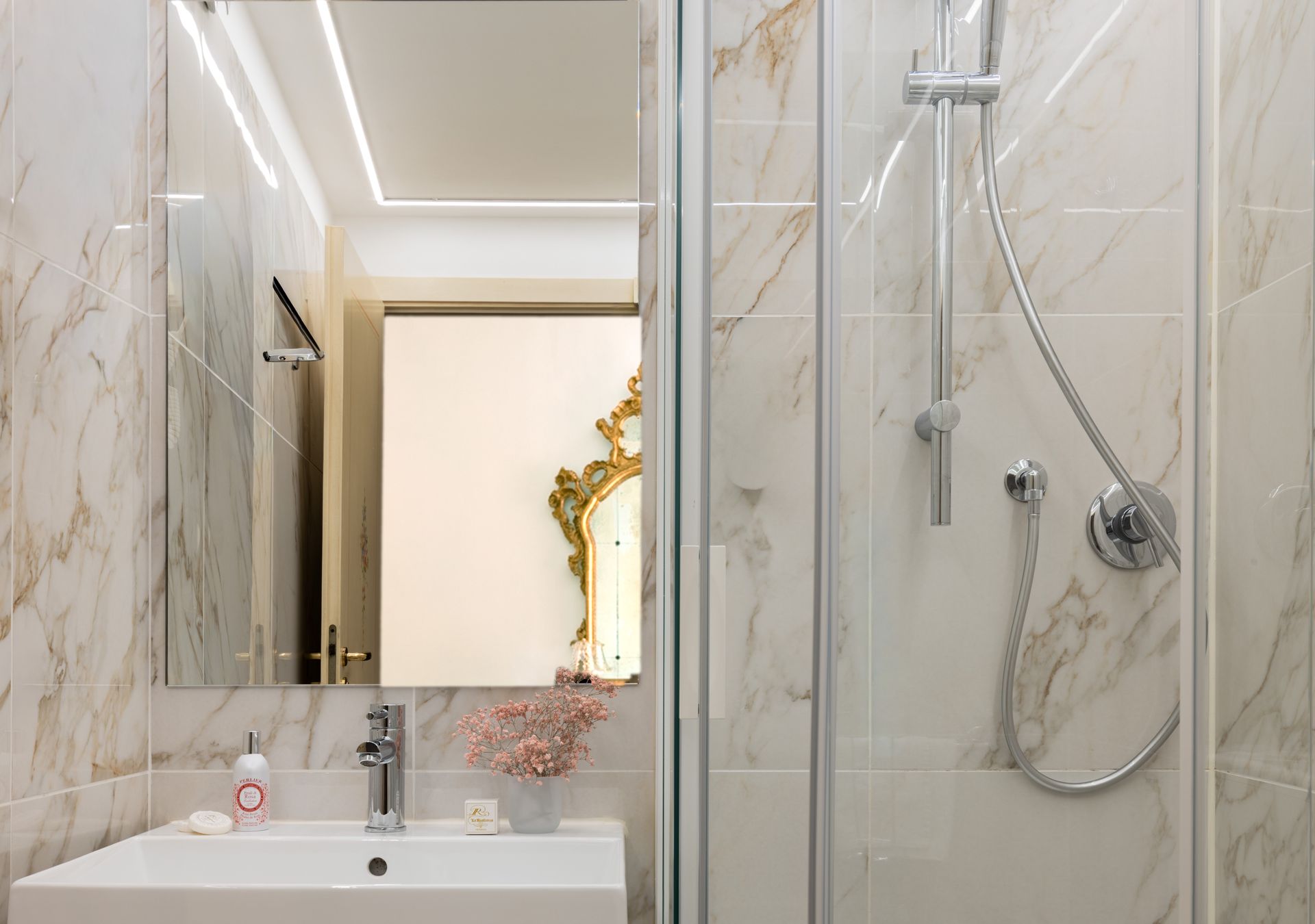Bagno moderno con pareti in marmo, lavabo con mobiletto, specchio e box doccia in vetro.