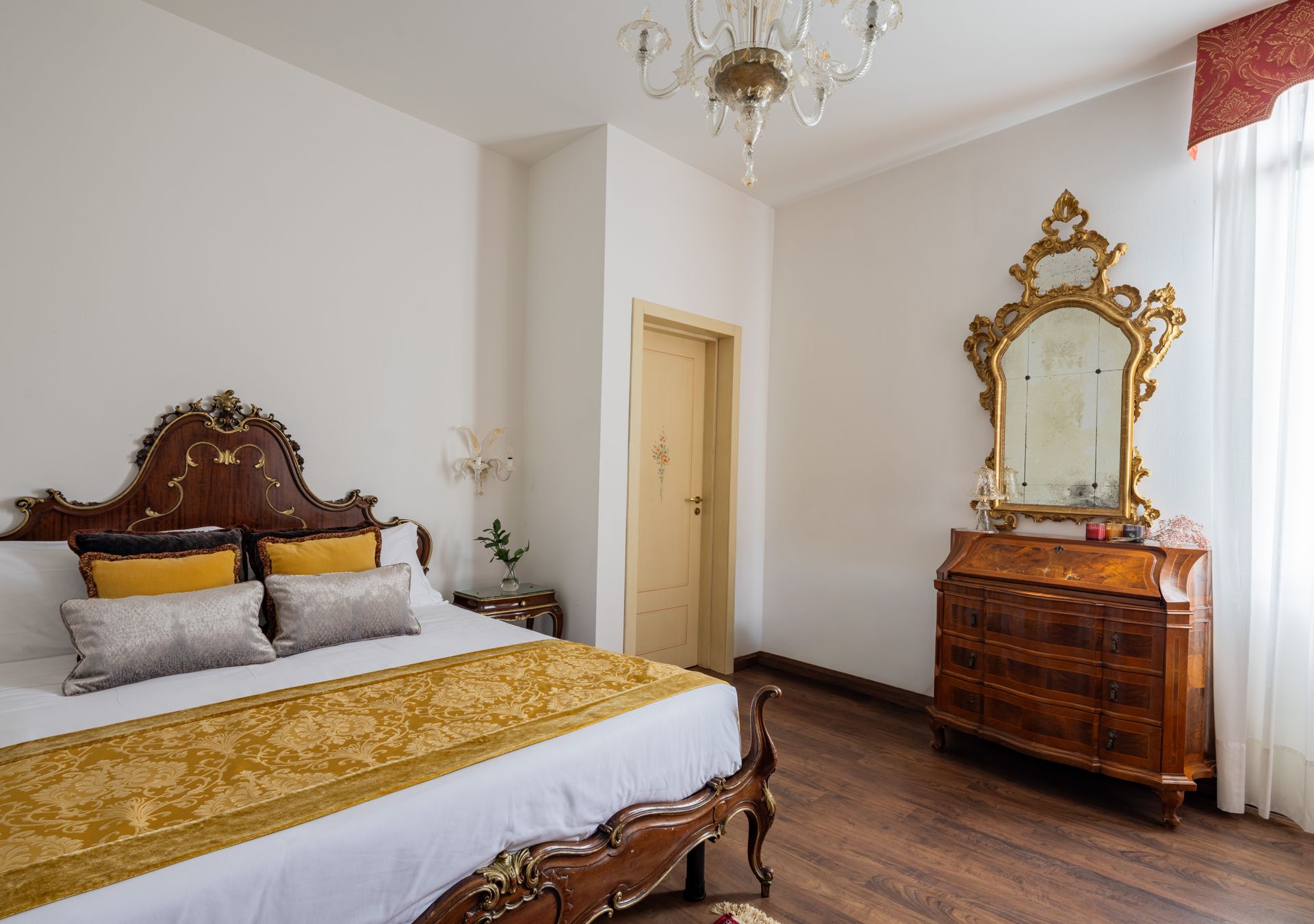 Luminosa camera da letto con letto decorato, biancheria da letto dorata, lampadario e comò vintage con specchio.