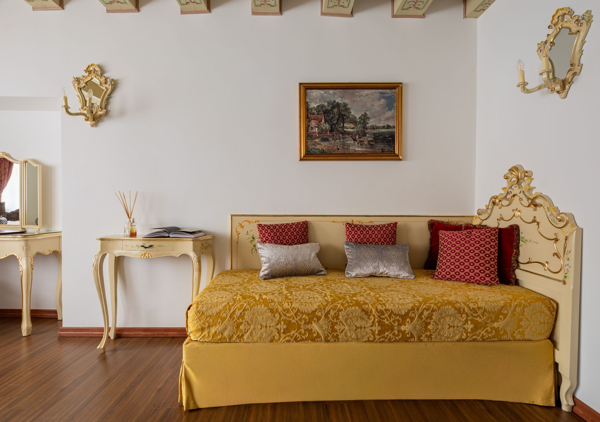 Elegante camera da letto con finiture dorate, letto con cuscini decorati, scrivania bianca e quadri appesi alle pareti.
