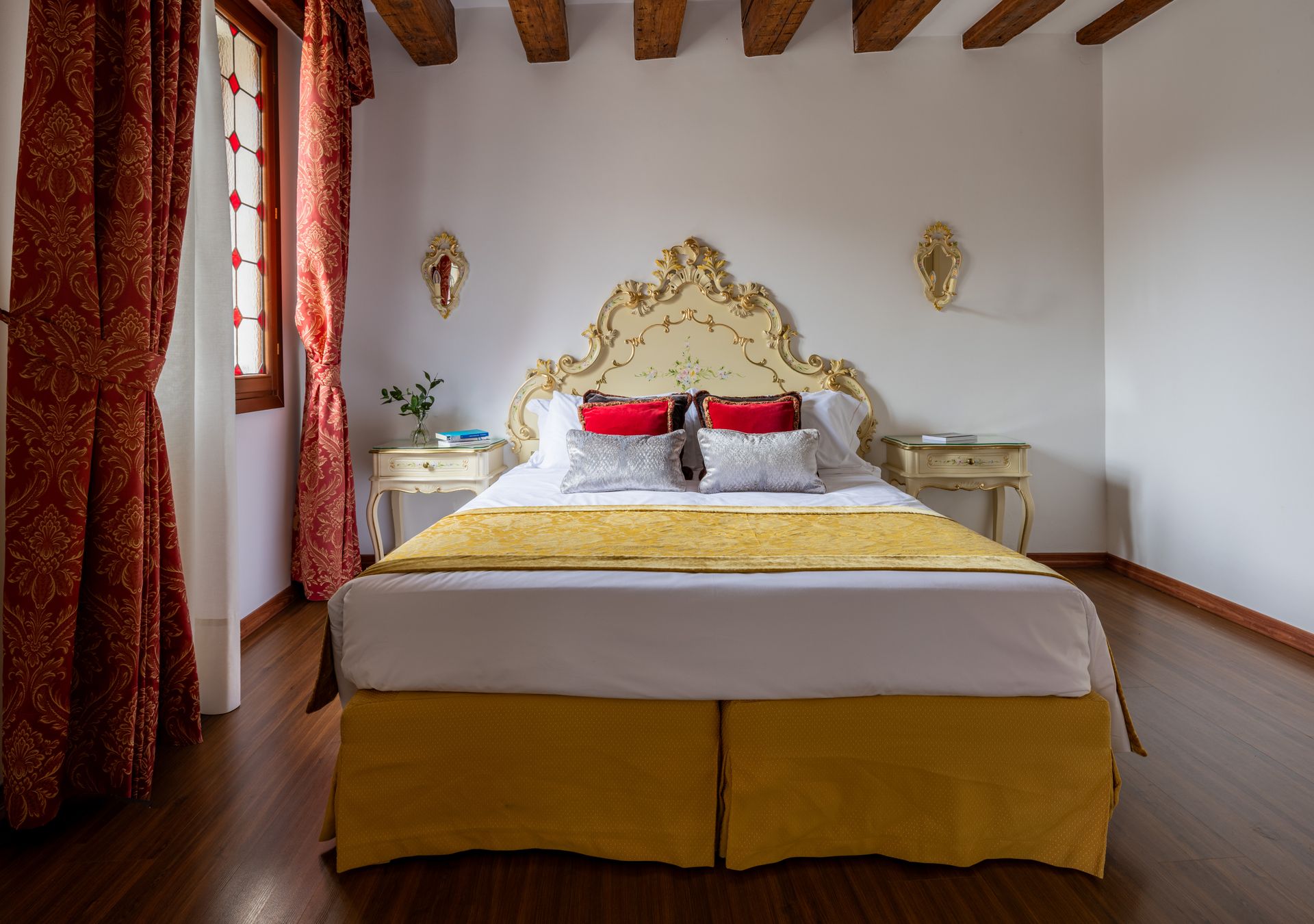 Elegante camera da letto con testiera dorata, tende rosse e copriletto bianco in una stanza rustica