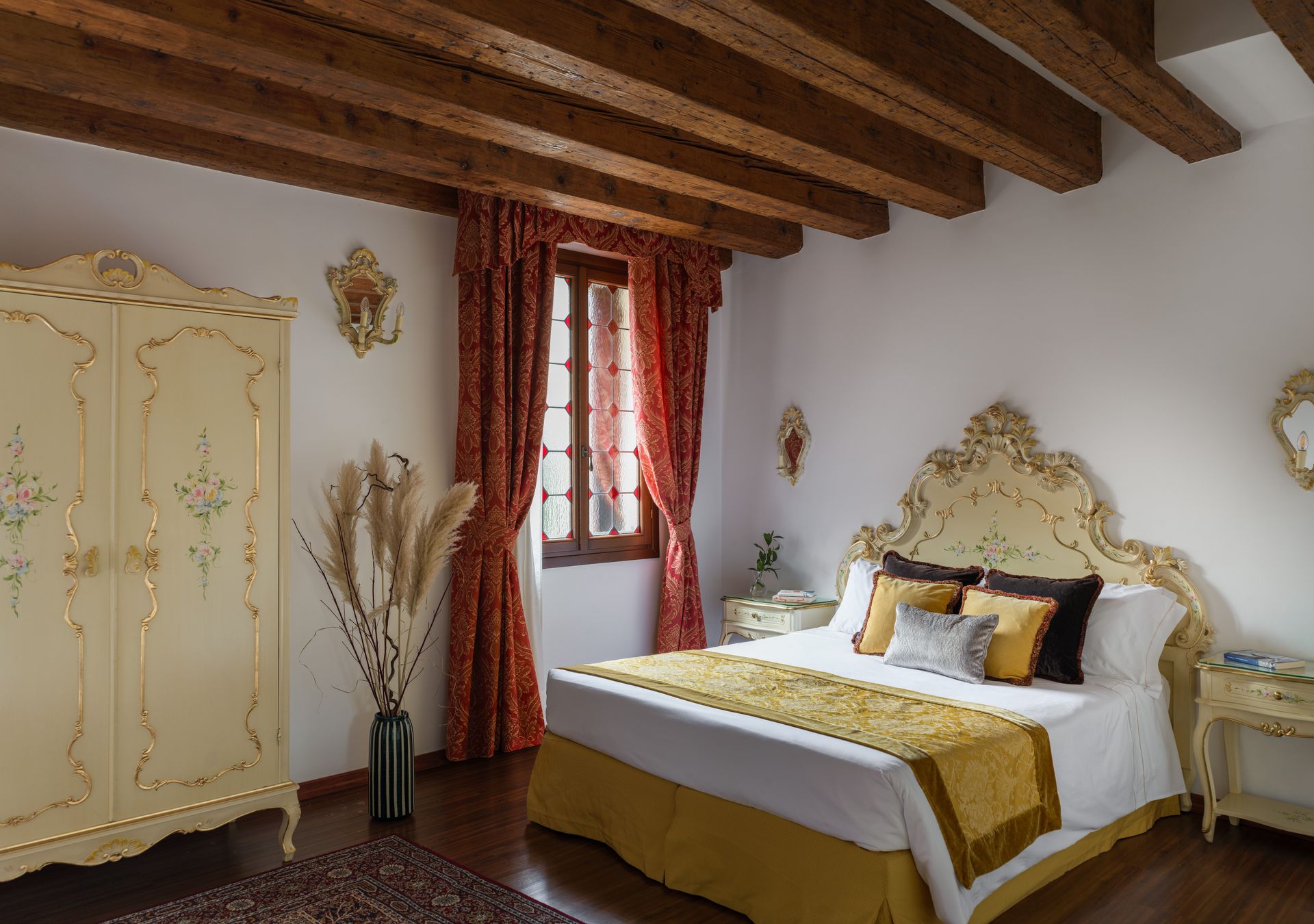 Elegante camera da letto in stile rustico con travi in ​​legno a vista, mobili color crema decorati e tende rosse.