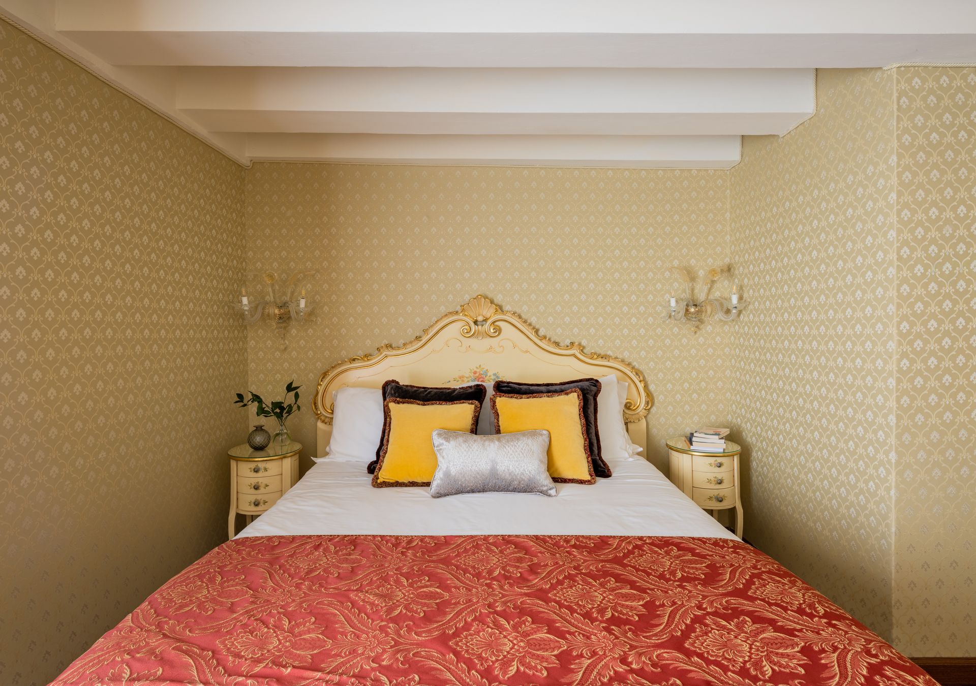 Elegante camera da letto con testiera dorata decorata, cuscini gialli e copriletto rosso.