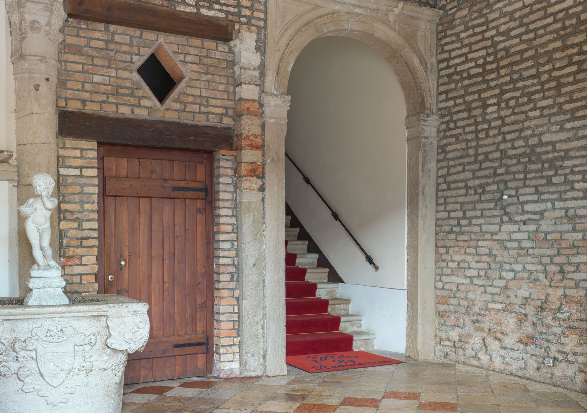 Interno in pietra con portale ad arco, porta in legno, scalinata rivestita di moquette rossa