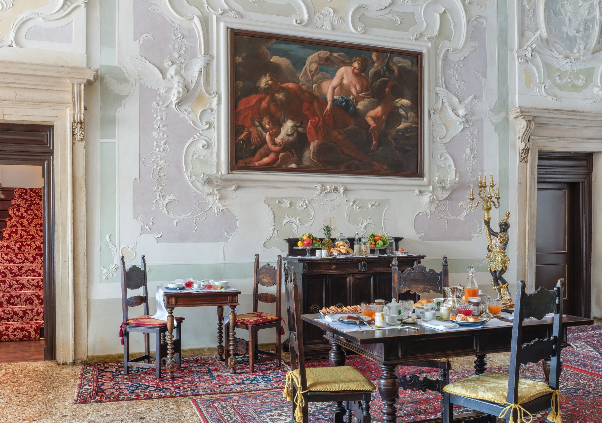 Elegante sala da pranzo con pareti bianche decorate, un grande quadro e un tavolo apparecchiato con fiori e piatti.