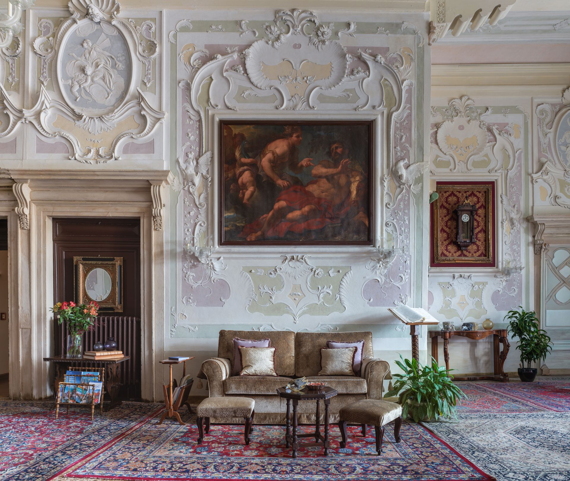 Elegante soggiorno con pareti bianche decorate, quadri classici, divani e tappeto rosso a motivi geometrici.