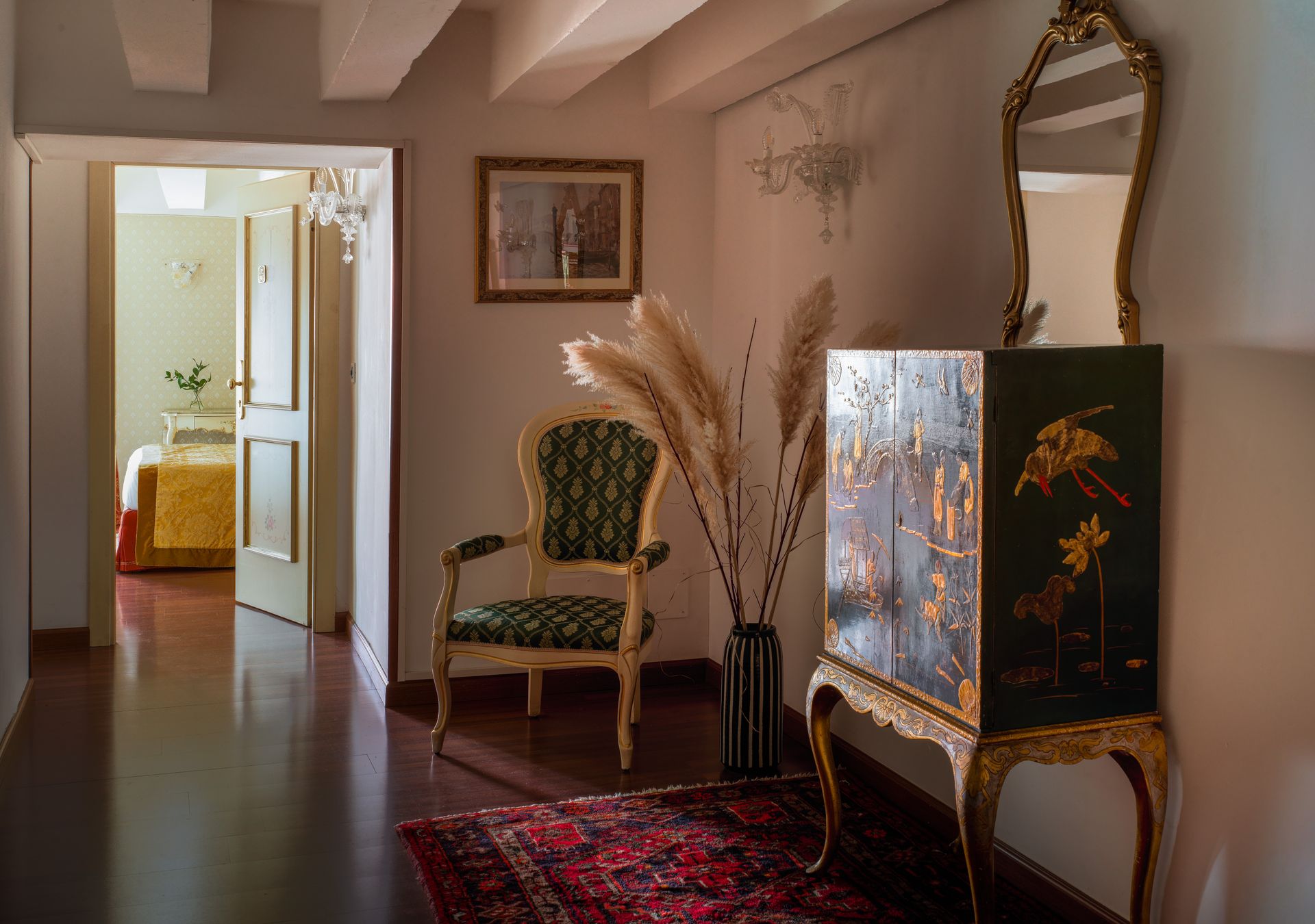Elegante corridoio con poltrona verde, paravento decorativo, tappeto rosso e vaso di fiori secchi.