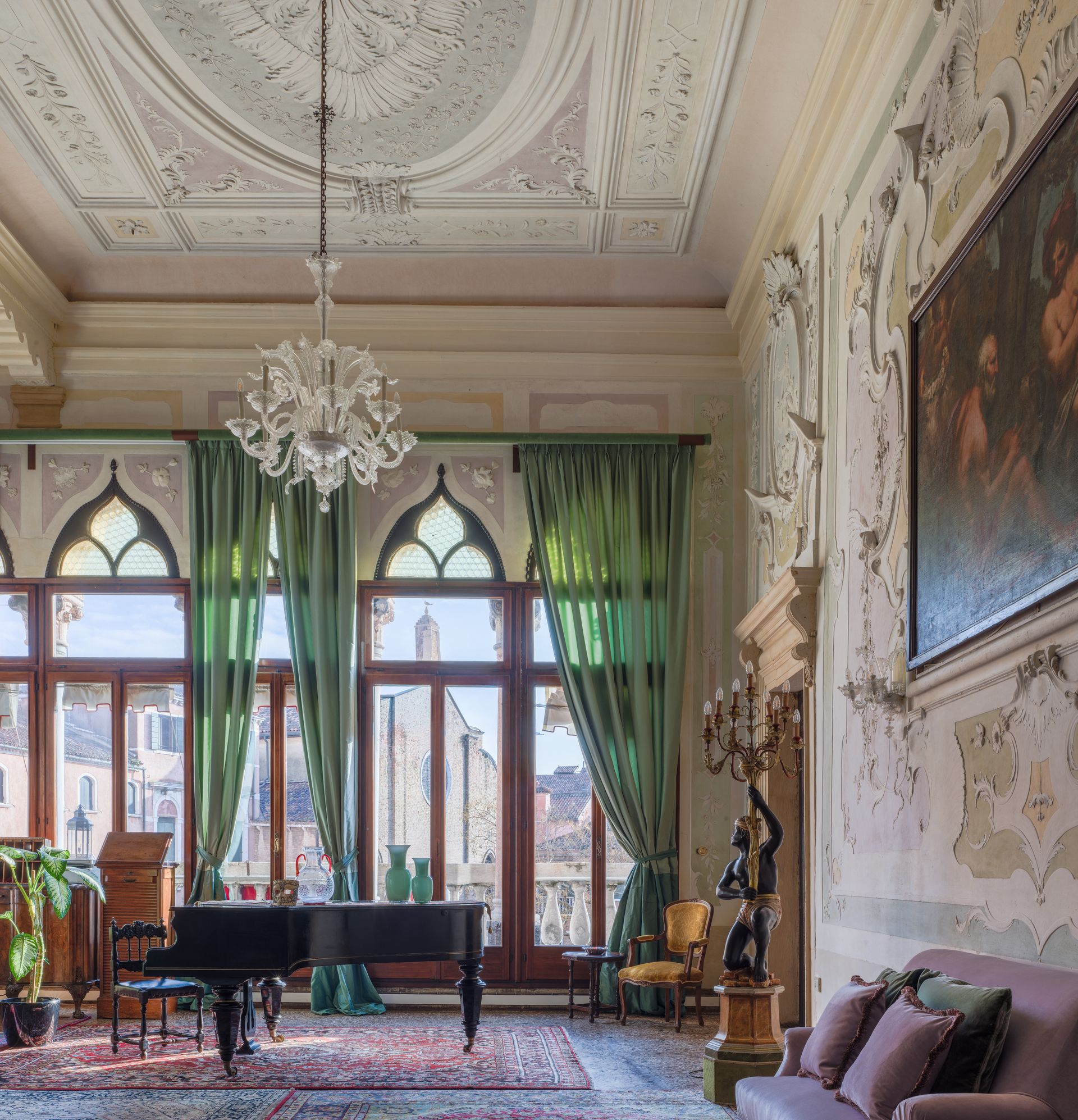 Elegante salotto luminoso con soffitto decorato, lampadario, pianoforte a coda, tende verdi e ampie finestre.
