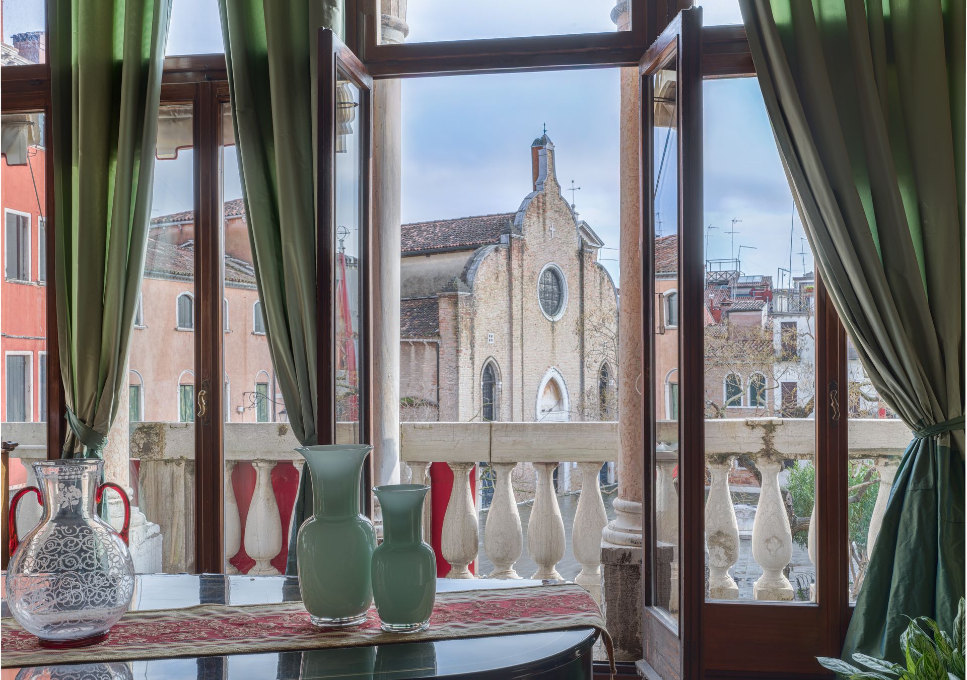 Vista attraverso la finestra di un caffè con tende verdi e vasi rossi, che si affaccia su una storica chiesa