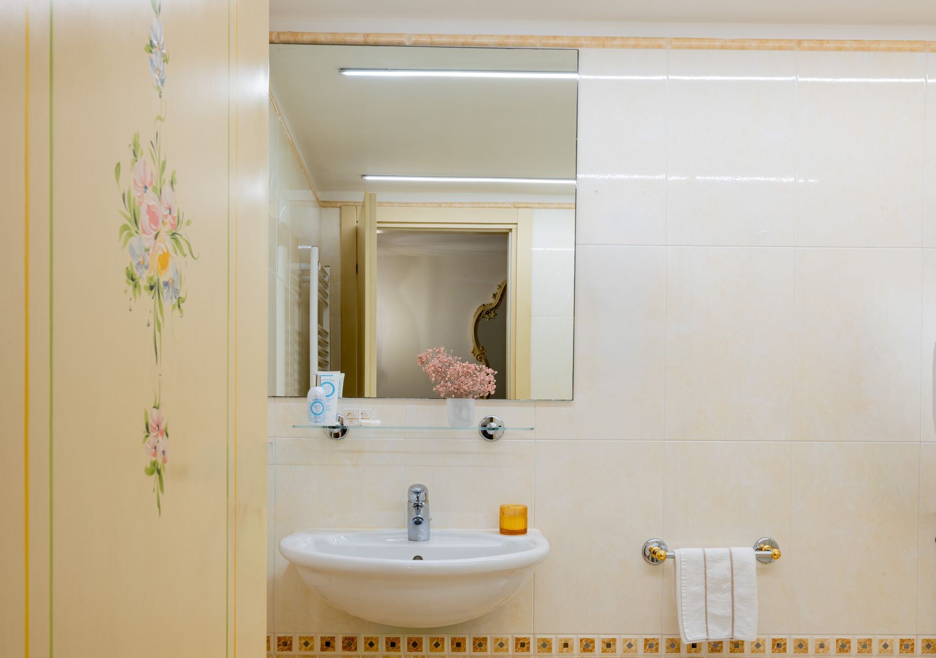Bagno luminoso color beige con lavabo, specchio, quadri e portasciugamani.