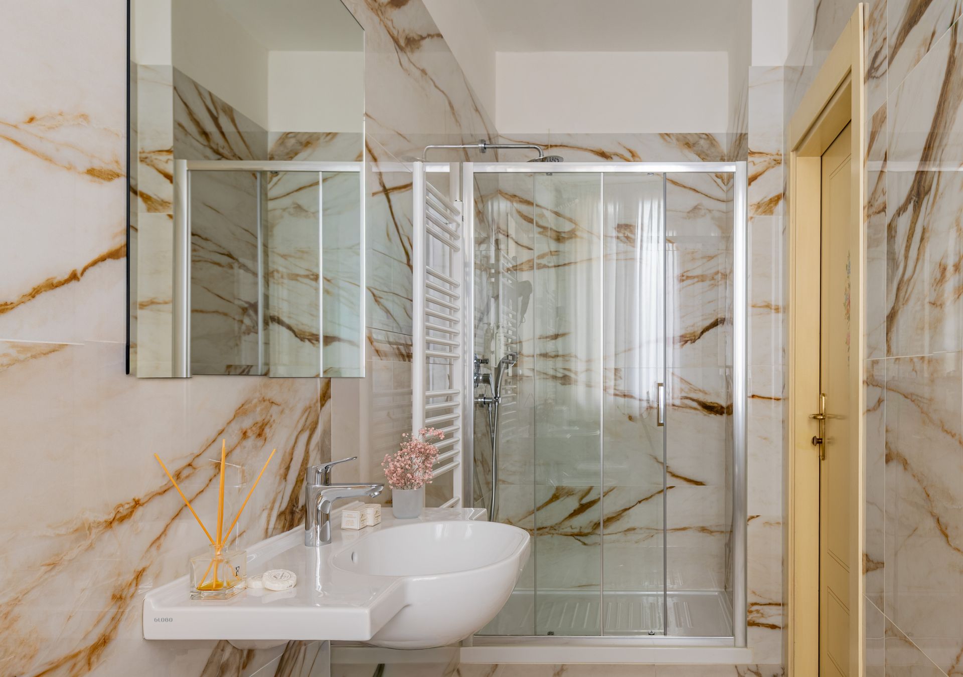 Bagno moderno con pareti in marmo, doccia in vetro, lavabo rotondo e dettagli dorati.