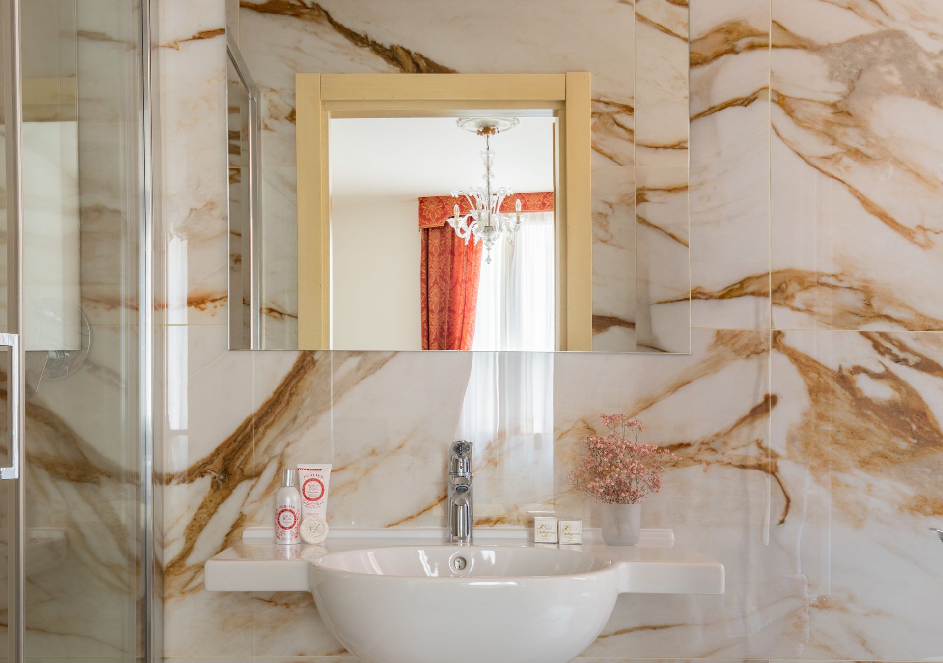 Bagno in marmo con specchio a parete, lavabo a ciotola bianco e tenda da doccia arancione riflessa nello specchio