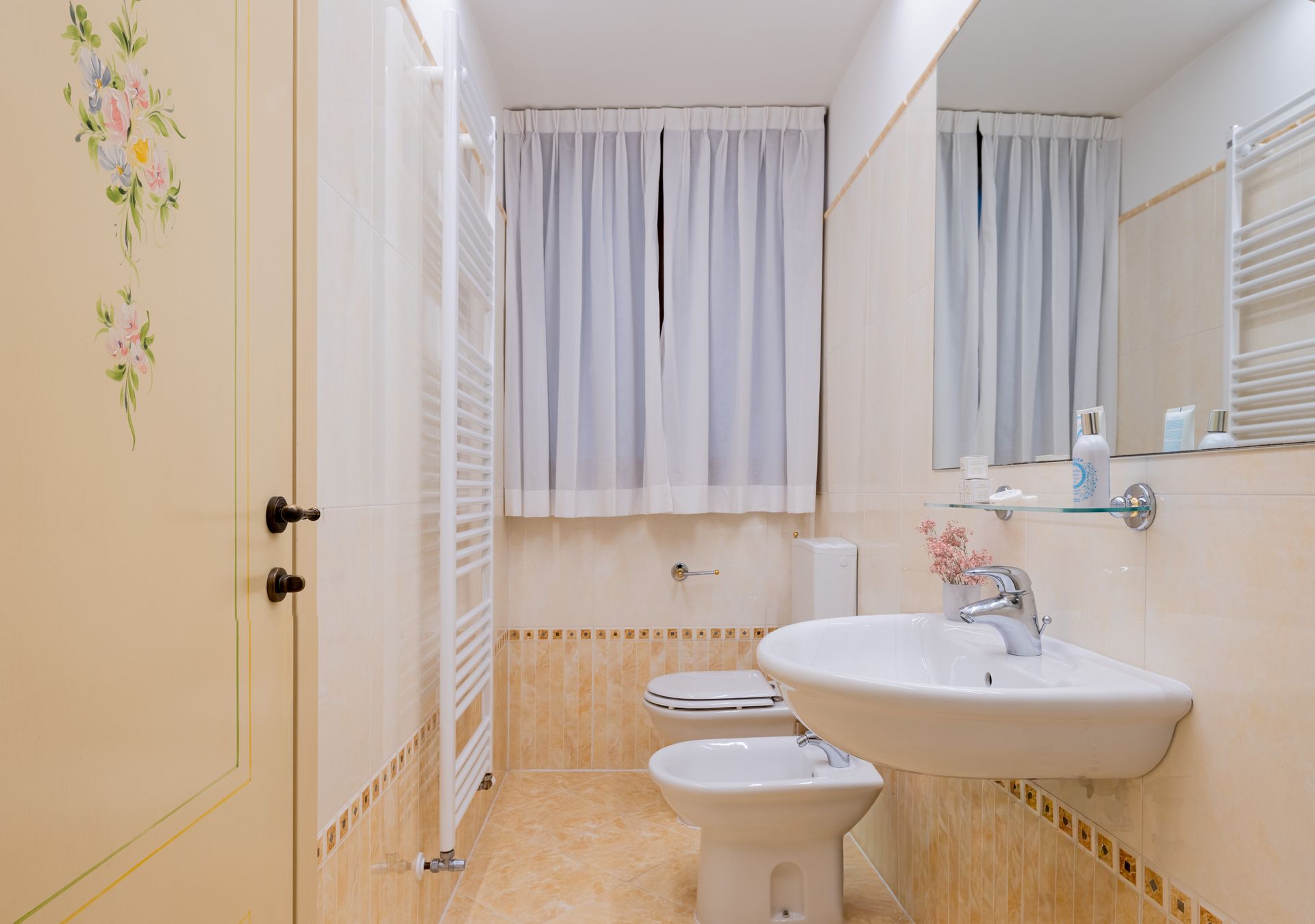 Bagno luminoso con lavabo, WC e tenda da doccia bianchi, e pareti rivestite con piastrelle beige.