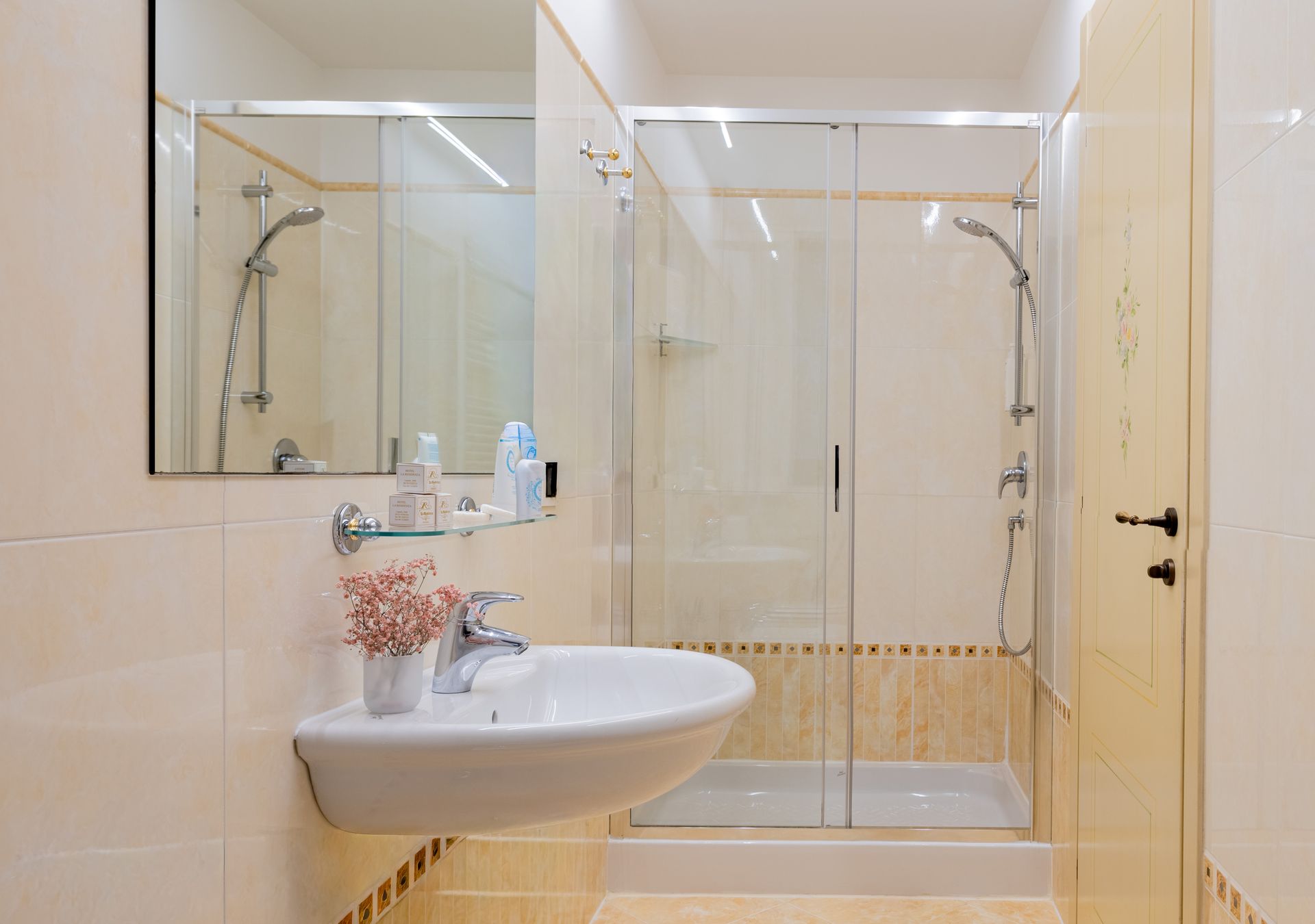 Bagno luminoso con doccia in vetro, lavabo bianco, specchio e piastrelle beige.