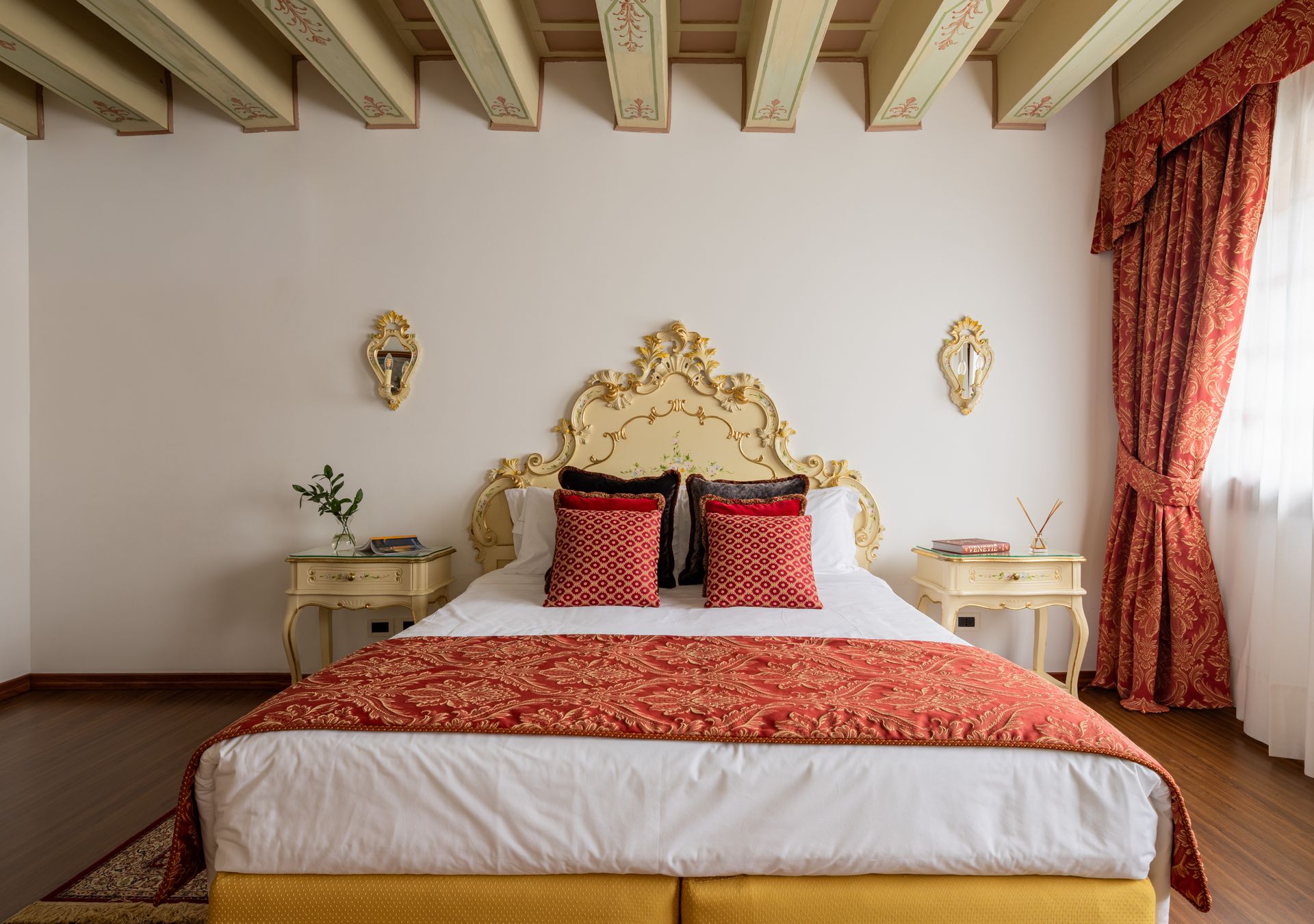 Elegante camera da letto con testiera dorata, biancheria da letto con motivi rossi e finestra con tende