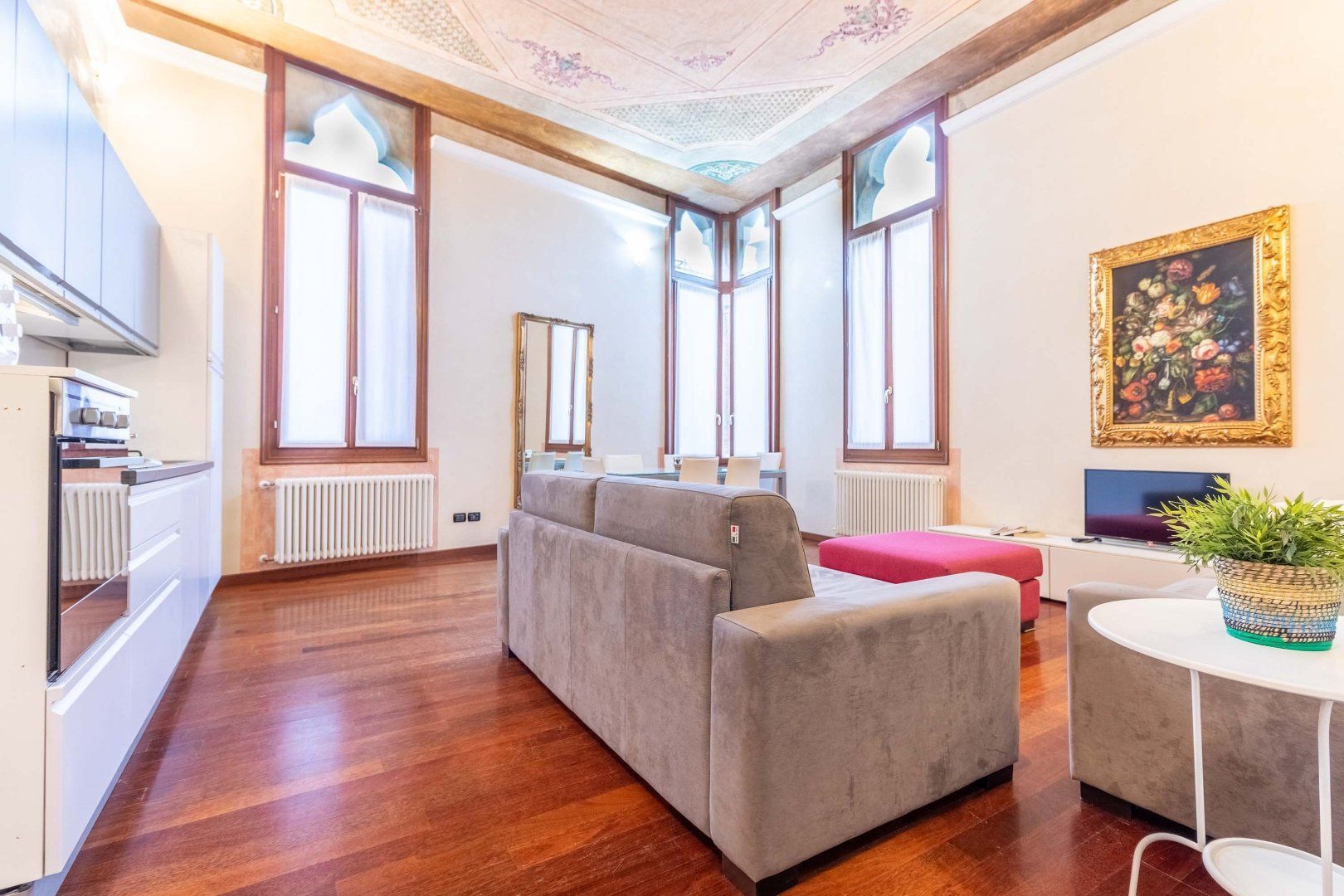 Salon lumineux avec parquet, canapé d'angle gris, grandes fenêtres et œuvres d'art murales colorées