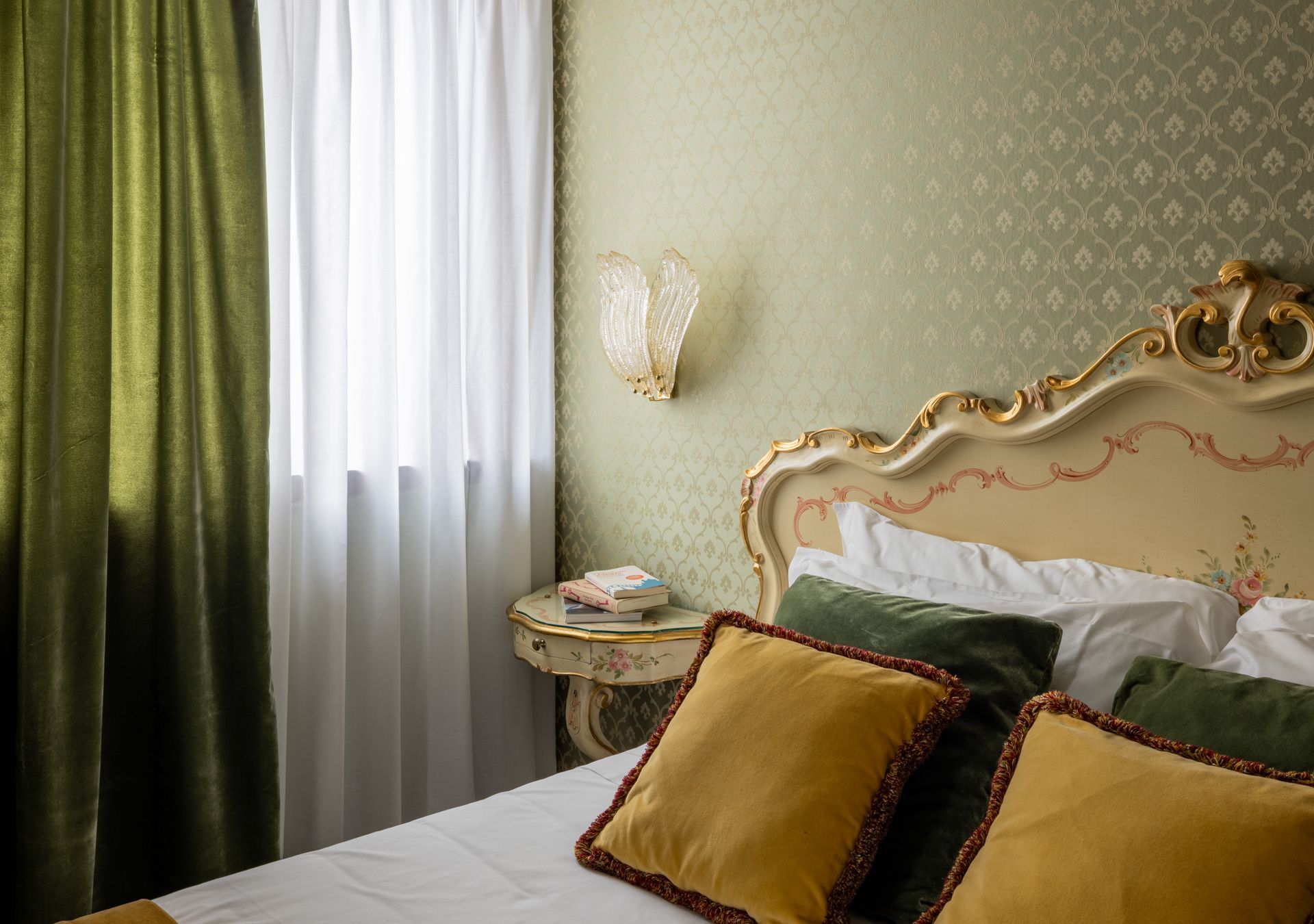 Elegant bedroom with ornate gold headboard, green curtains, sheer drapes, and white bedding with mustard pillows