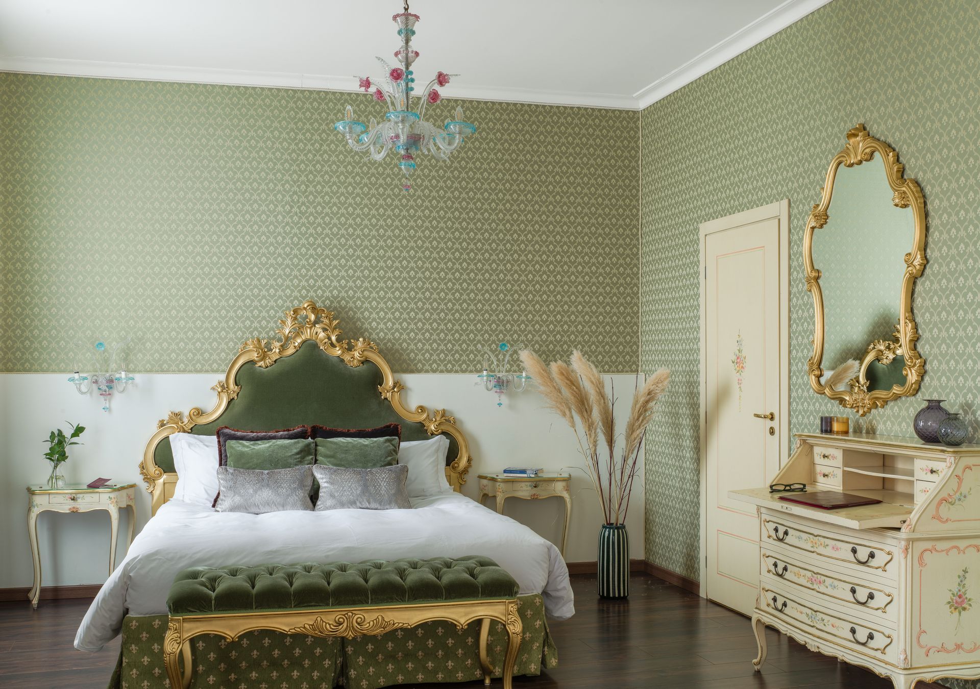 Elegant bedroom with green wallpaper, gold ornate bed, chandelier, and cream dresser with mirror