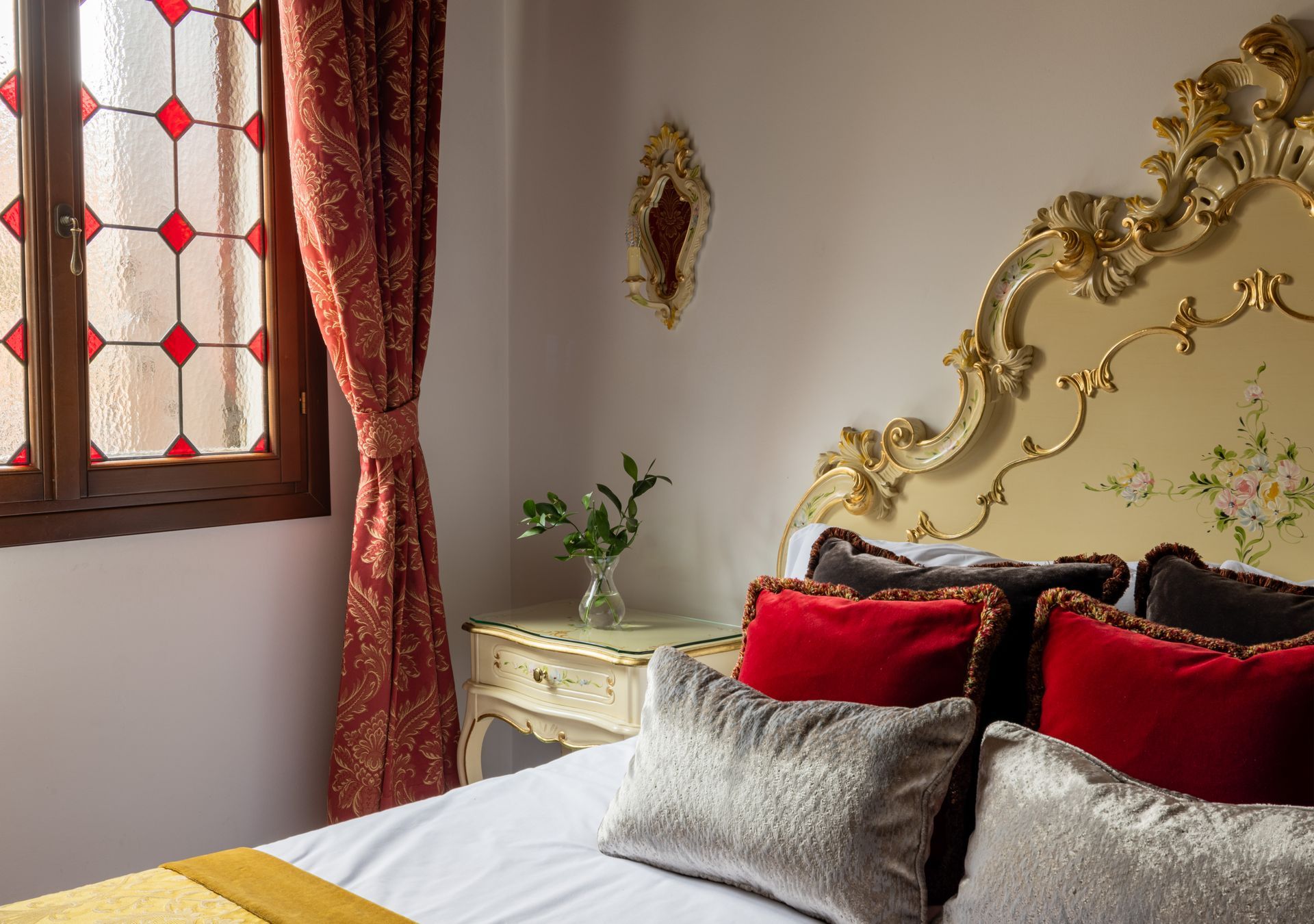 Elegant bedroom with ornate gold headboard, red curtains, and a window with patterned glass