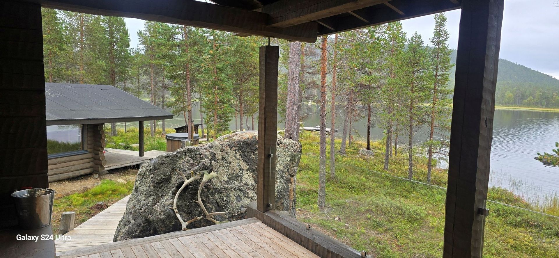 View from a wooden porch towards a lake and trees, with a small cabin to the left.