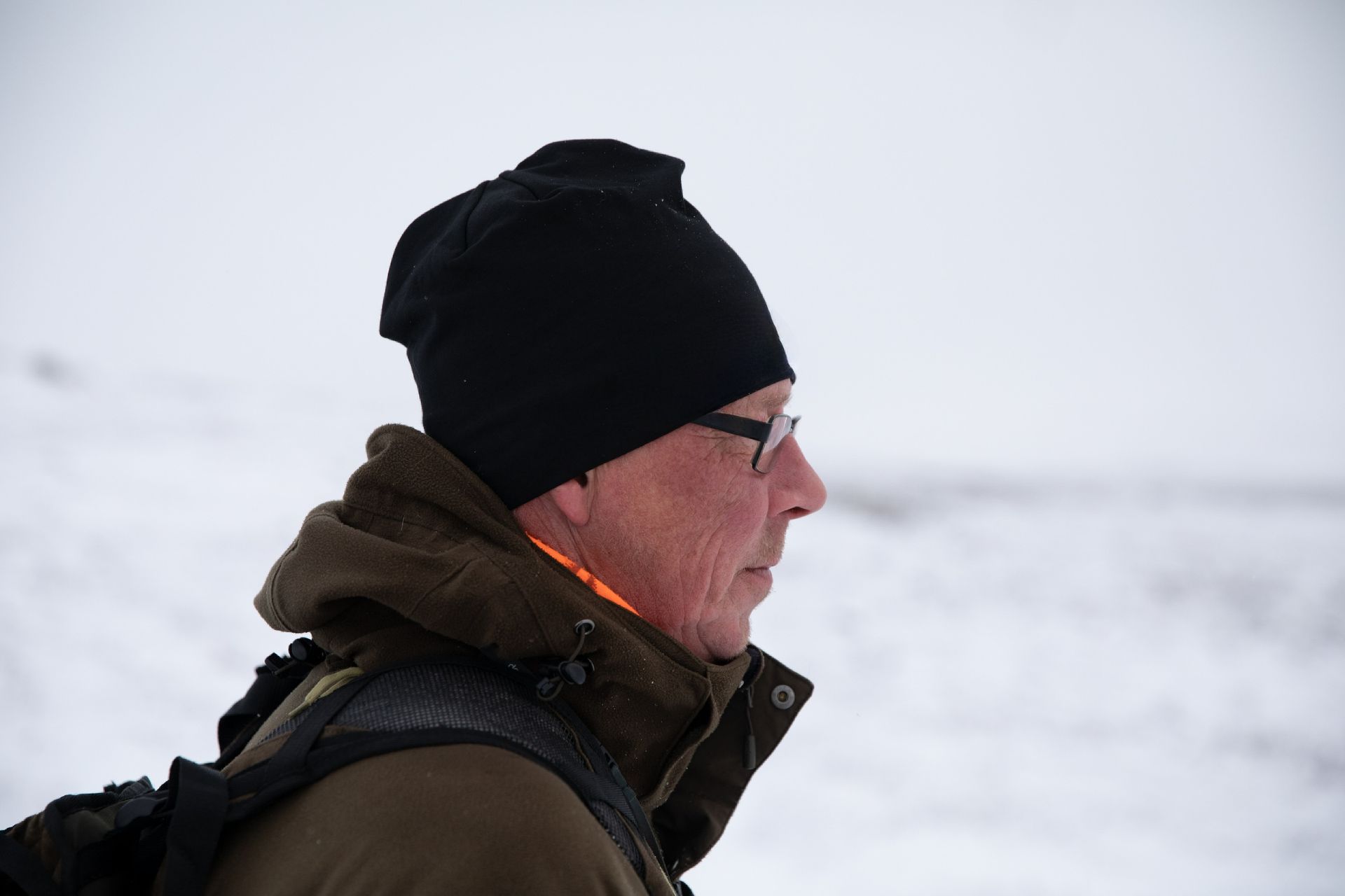 A man wearing a black hat and glasses is standing in the snow.