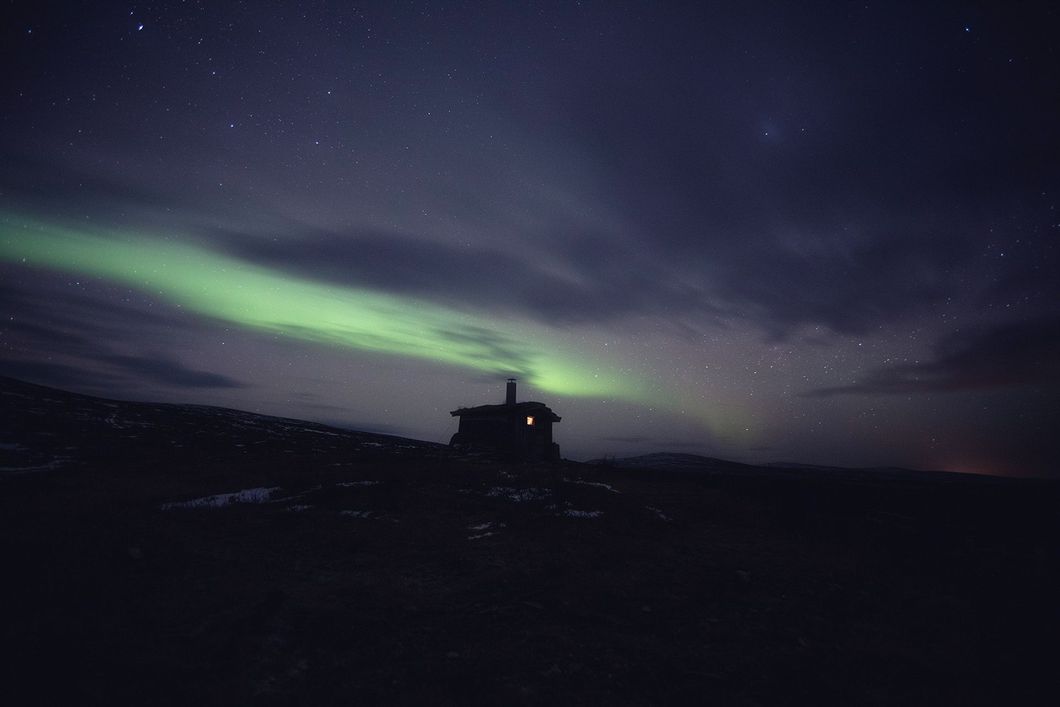 Silhouette of a small cabin under a starry night sky with green aurora borealis.