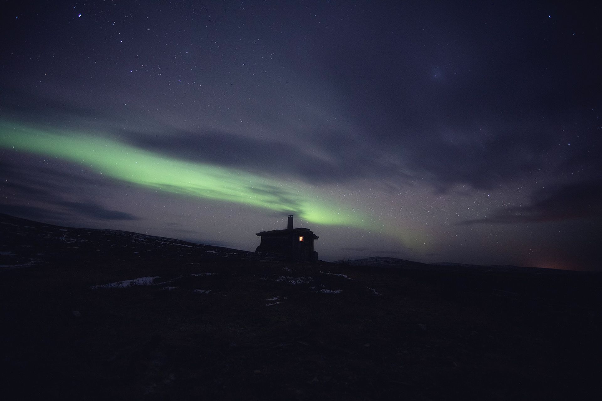 A house is silhouetted against the aurora borealis in the night sky.
