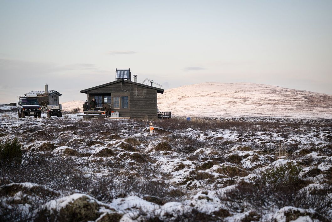 Cabin in a snowy landscape, with a vehicle parked nearby, under a soft sky.