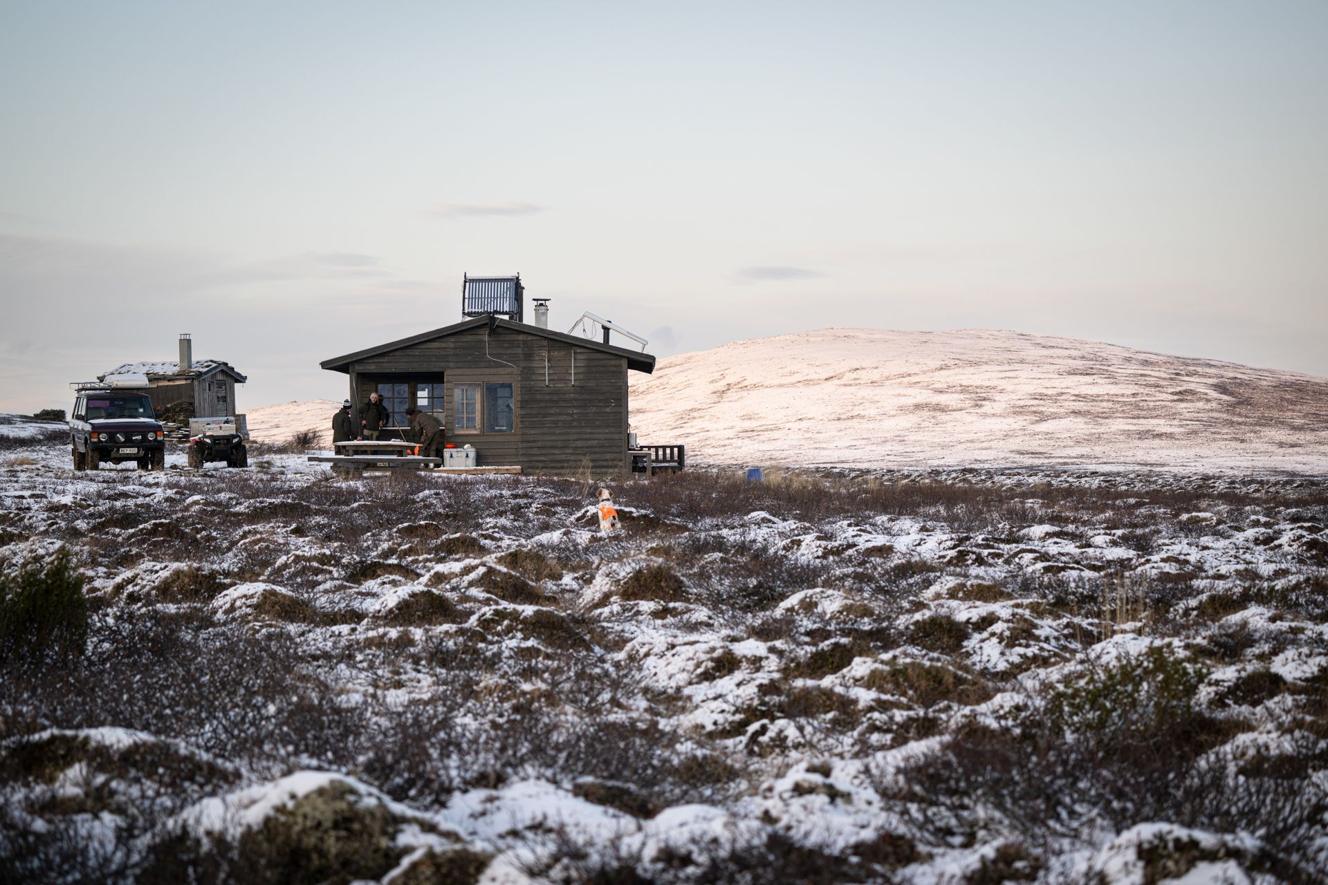 A small house is sitting in the middle of a snowy field.
