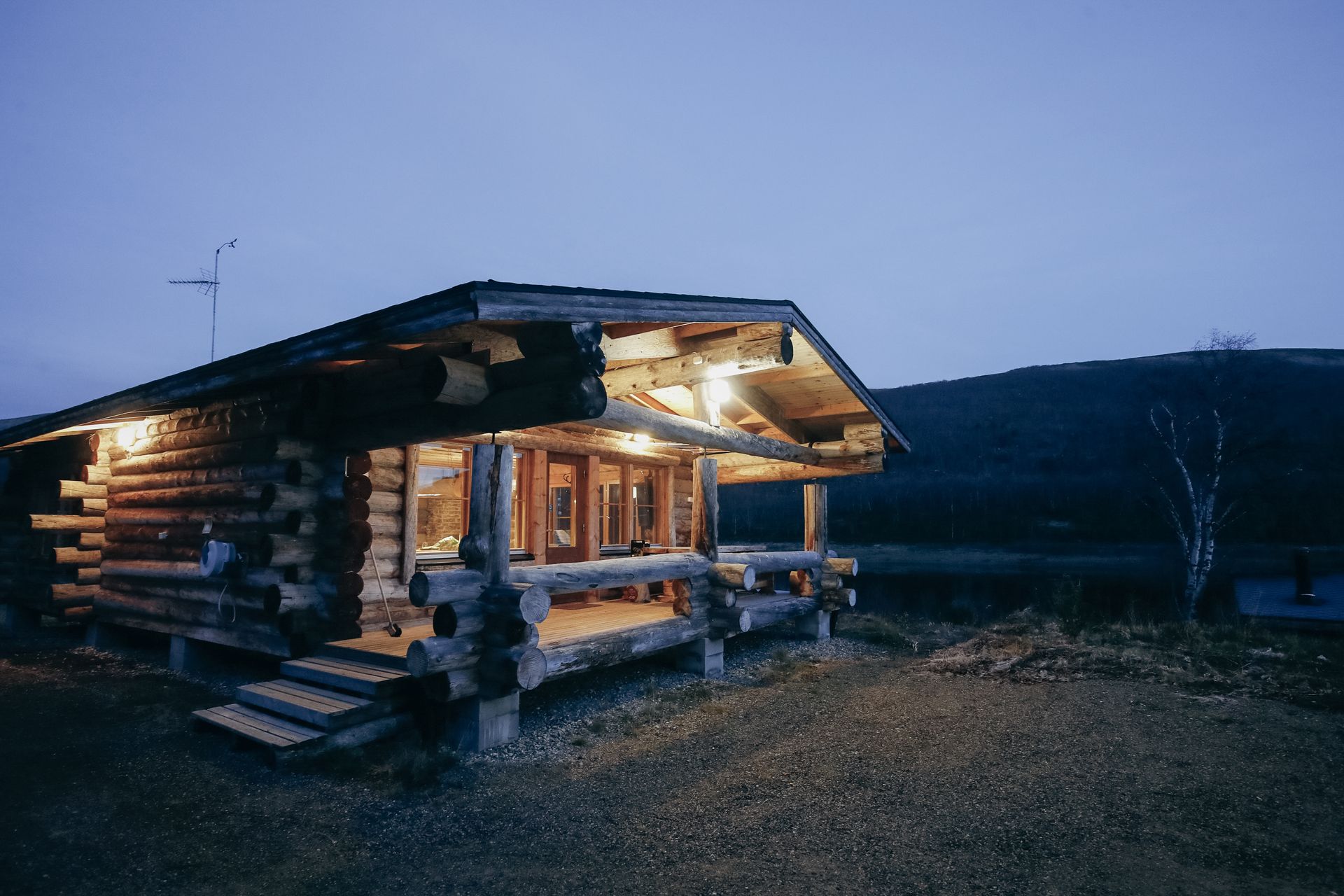 Rustic log cabin lit warmly at dusk in a dark, open landscape
