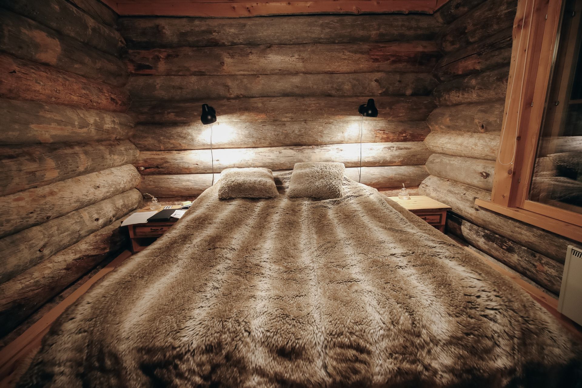 Cozy log cabin bedroom with a large bed, fur blanket, and warm wall lamps