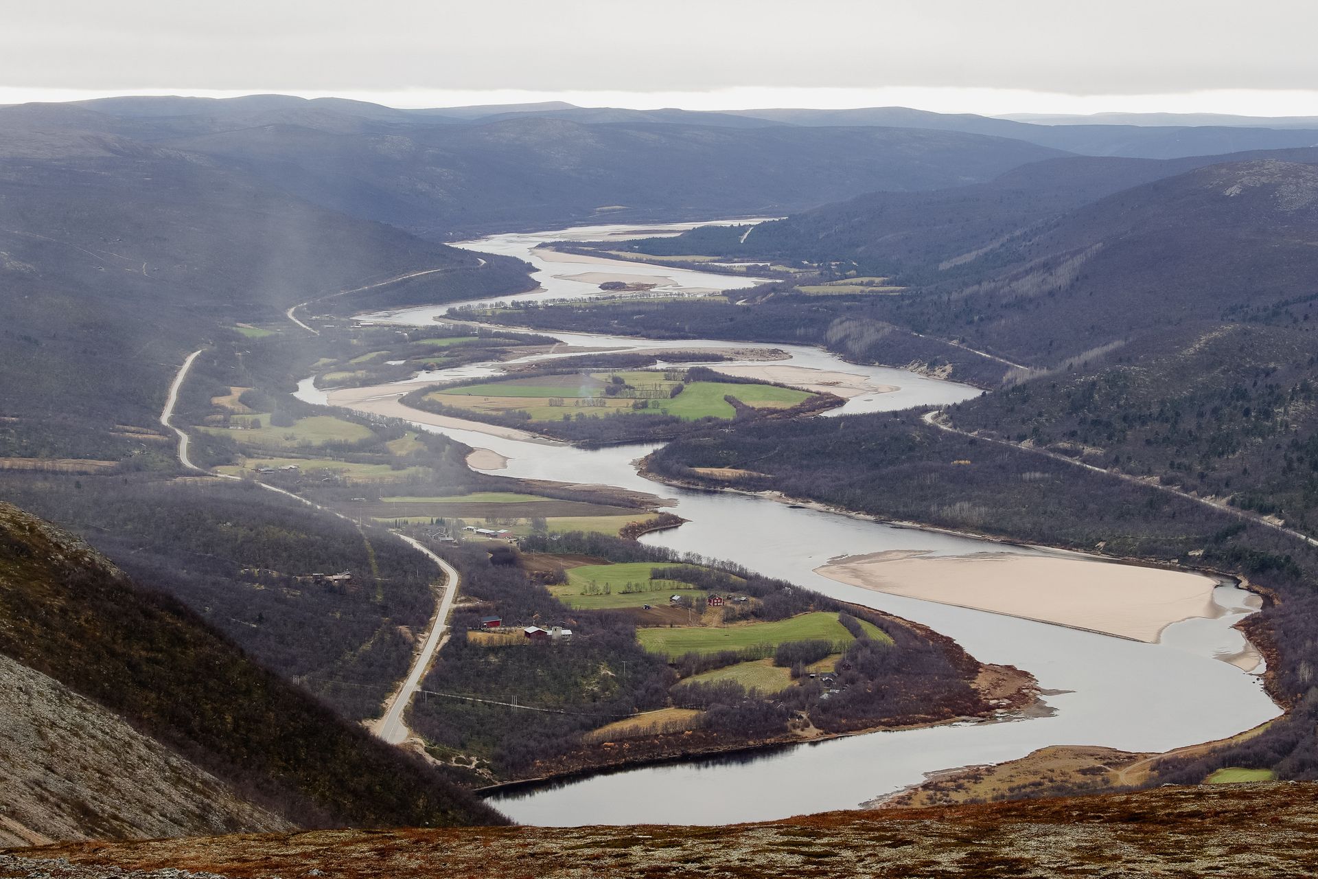 Winding river through a green valley under cloudy skies, seen from a high hillside viewpoint