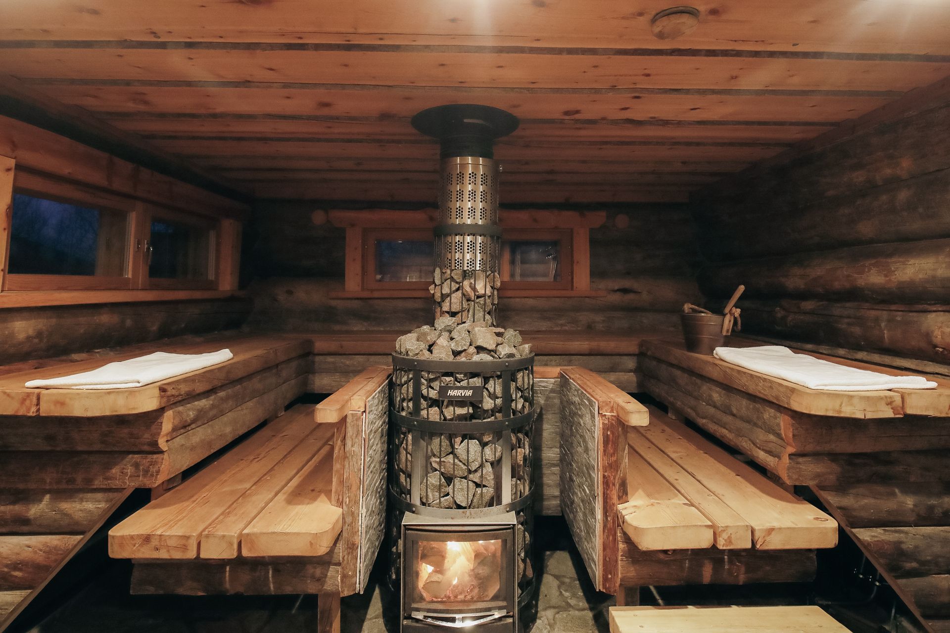 Rustic wooden sauna interior with benches and a central stove/heater under a low cedar ceiling