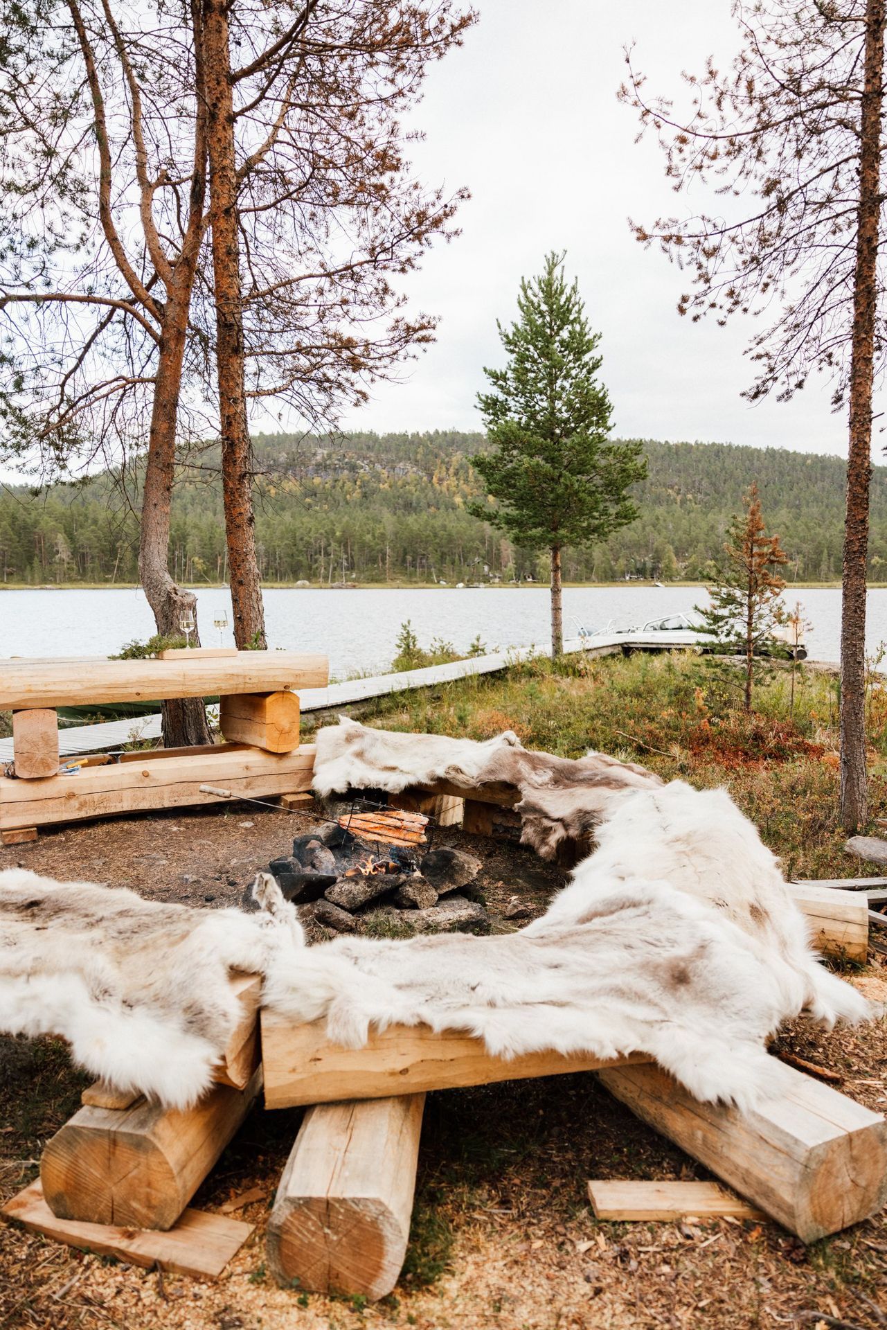 A wooden picnic table with a fire pit in the middle of a forest.