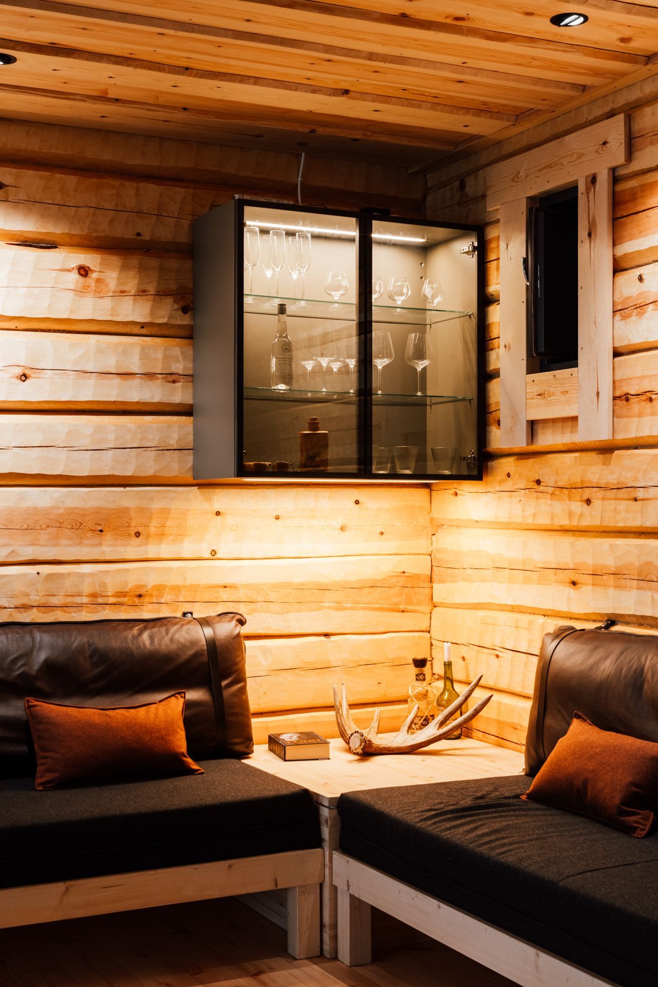 A living room in a log cabin with two couches and a glass cabinet.