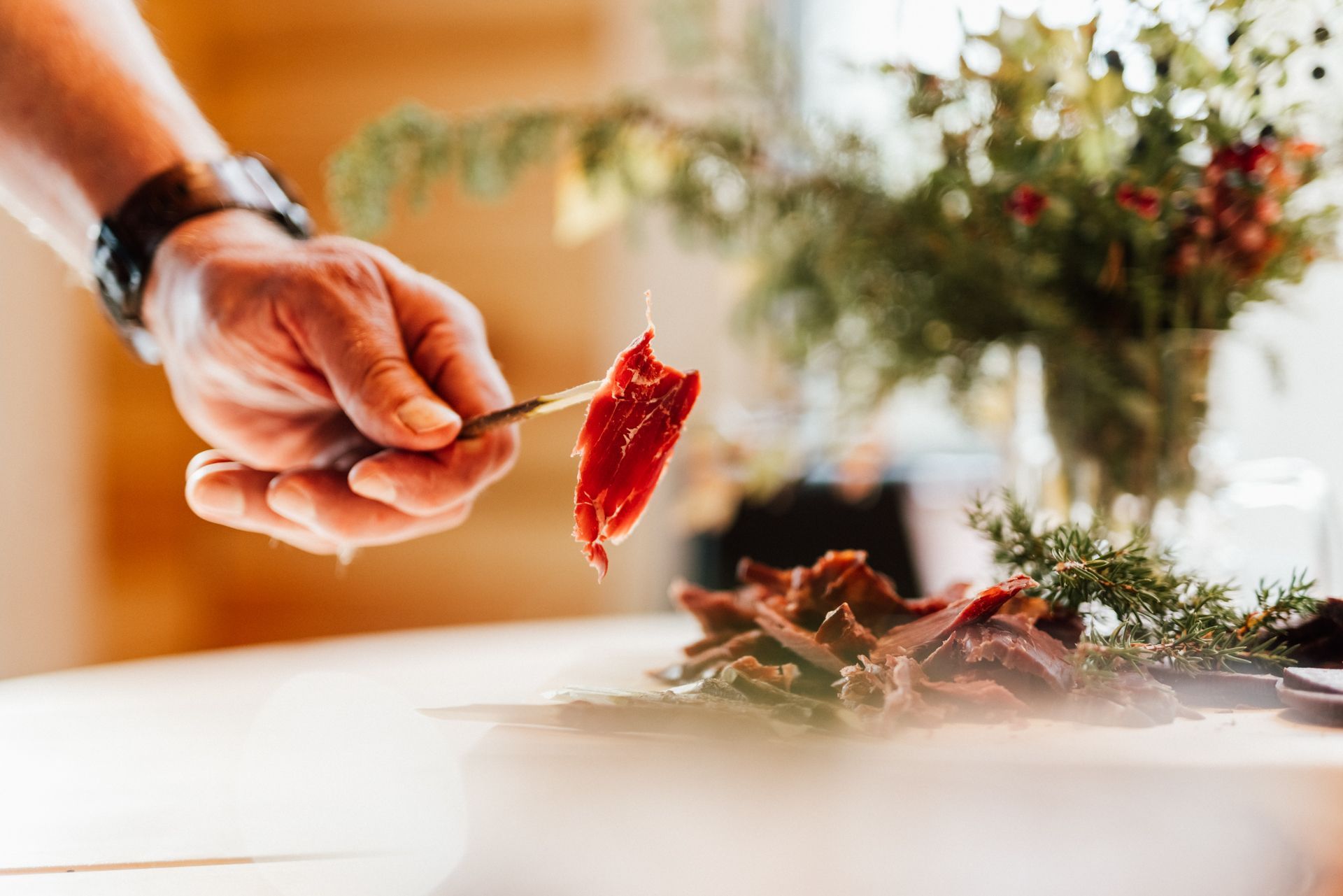 A person is holding a piece of meat on a toothpick over a plate of food.