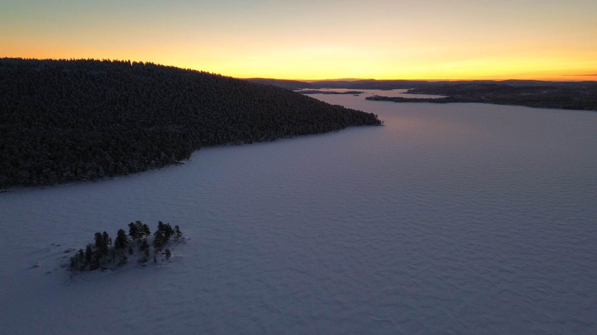 An aerial view of a snowy lake with a sunset in the background.