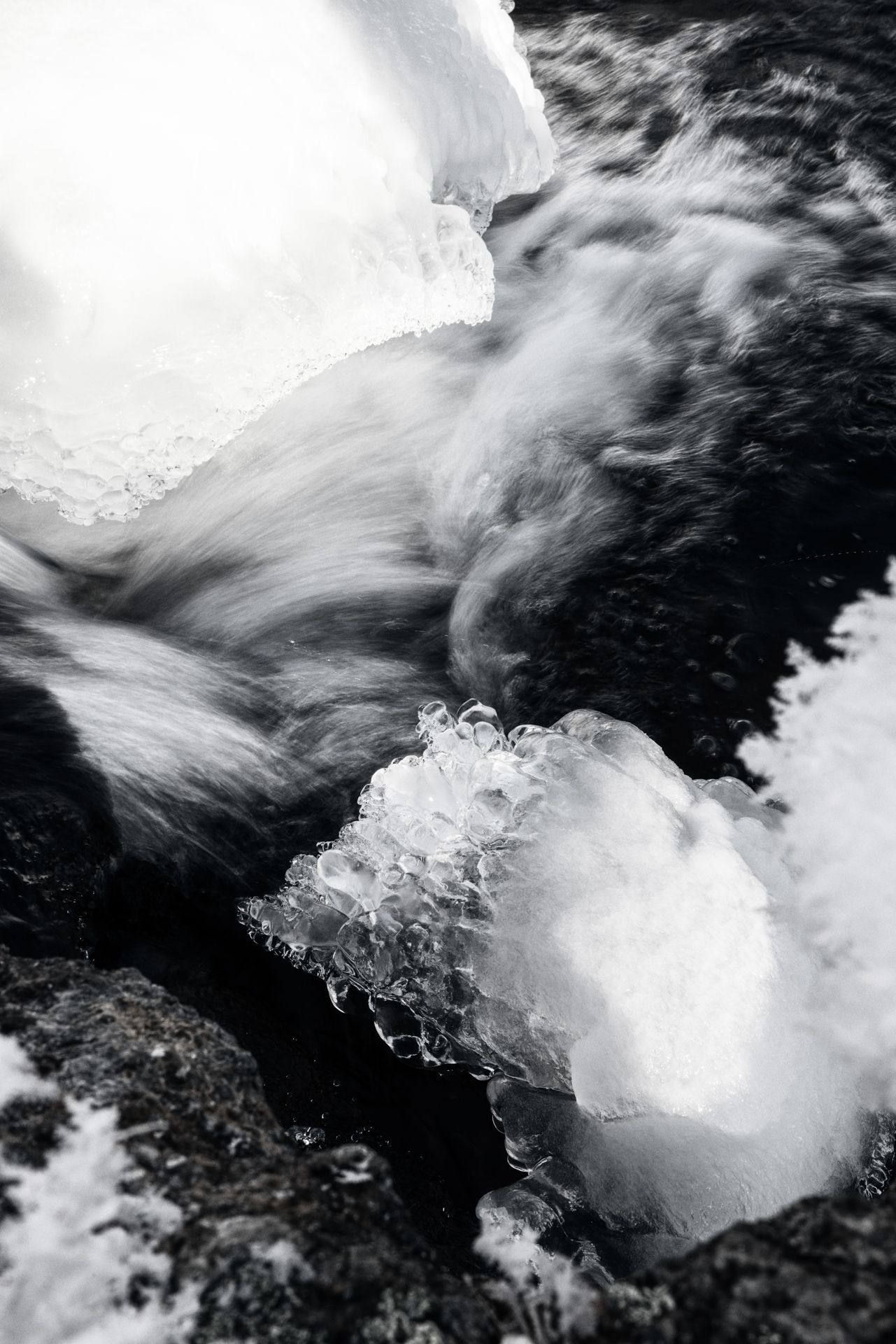 Rushing water through rocks, partially frozen. Ice chunks and blurred motion indicate cold temperatures.