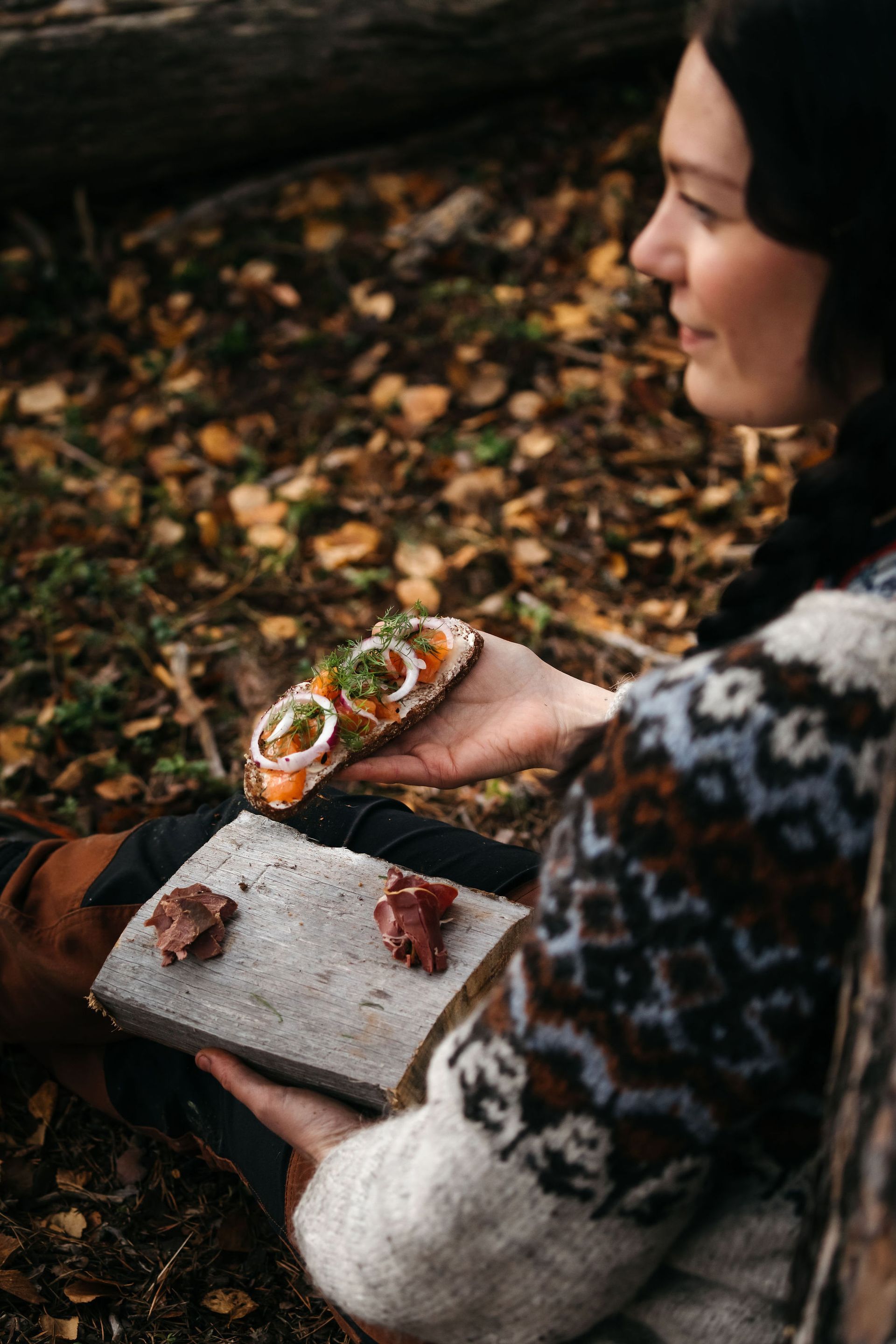 A woman is sitting on the ground holding a plate of food.